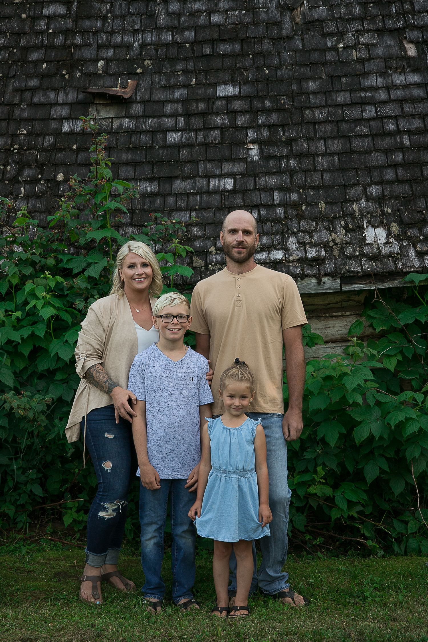 A group stands together against a dark shingled wall with green foliage.