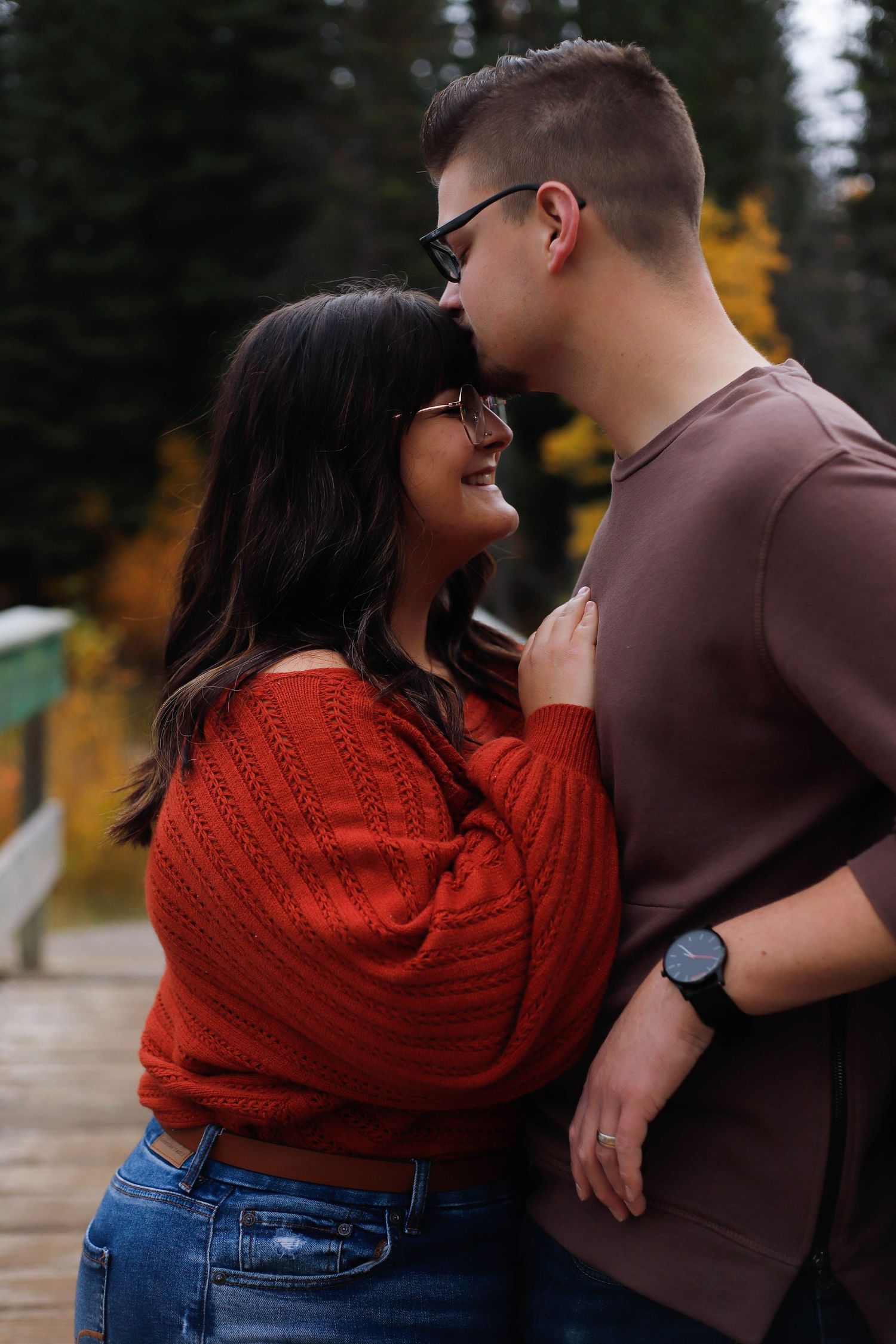 Romantic couple in casual attire share intimate moments outdoors, with woman wearing bright red sweater.
