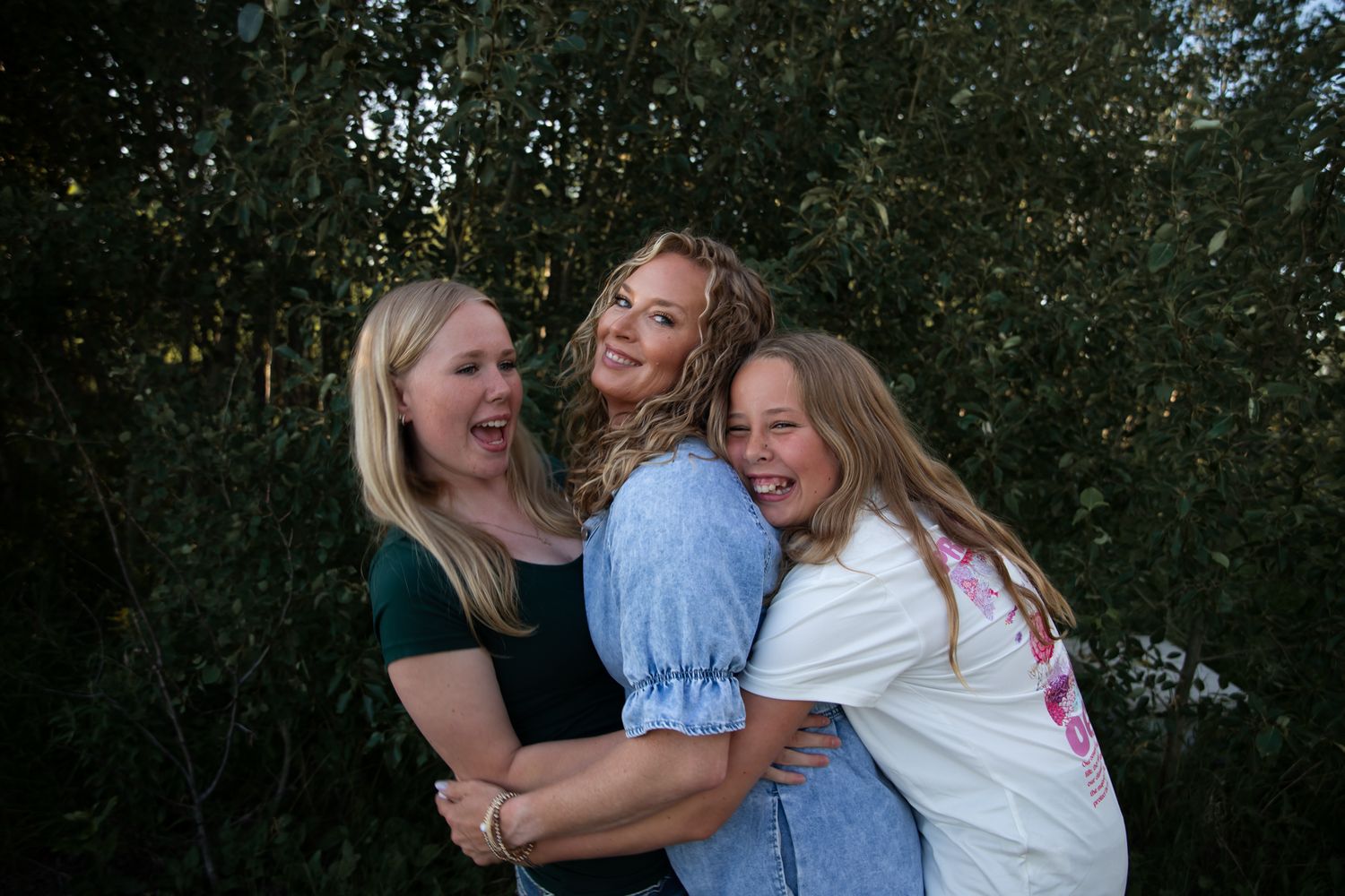 Three people share an energetic group hug while laughing together outdoors.