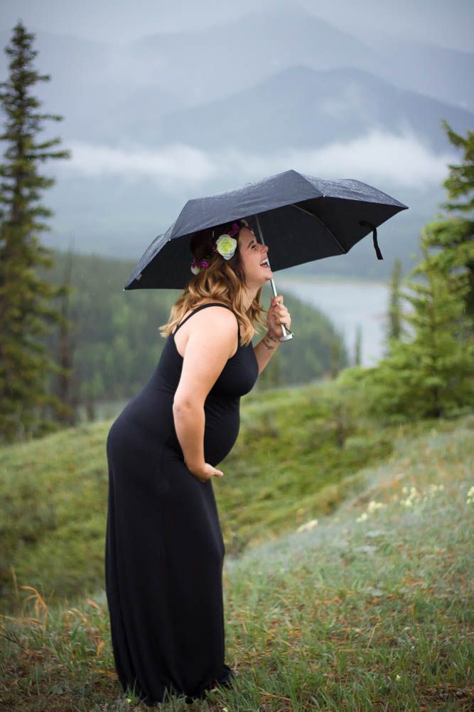 Woman with black umbrella poses elegantly on mountainside with foggy valley views.