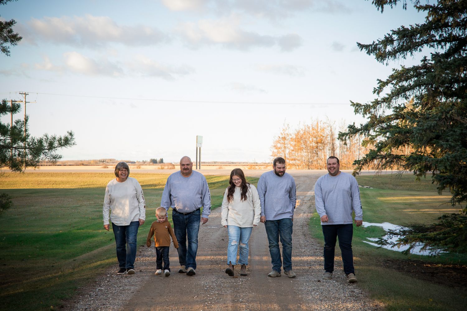 Family members walking together outdoors with pine trees and cloudy sky in background.