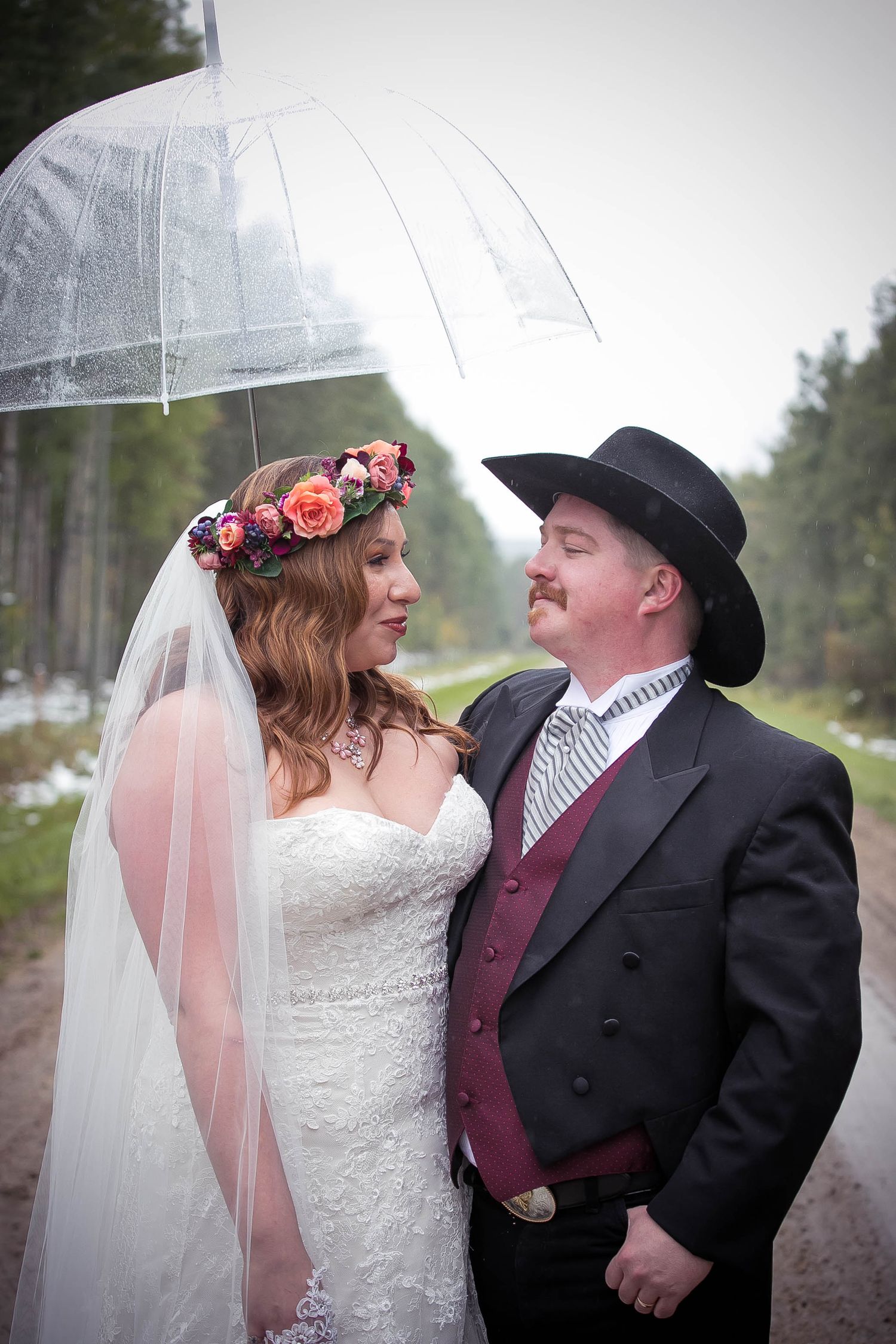 A couple shares an intimate moment under a clear umbrella on their wedding day.