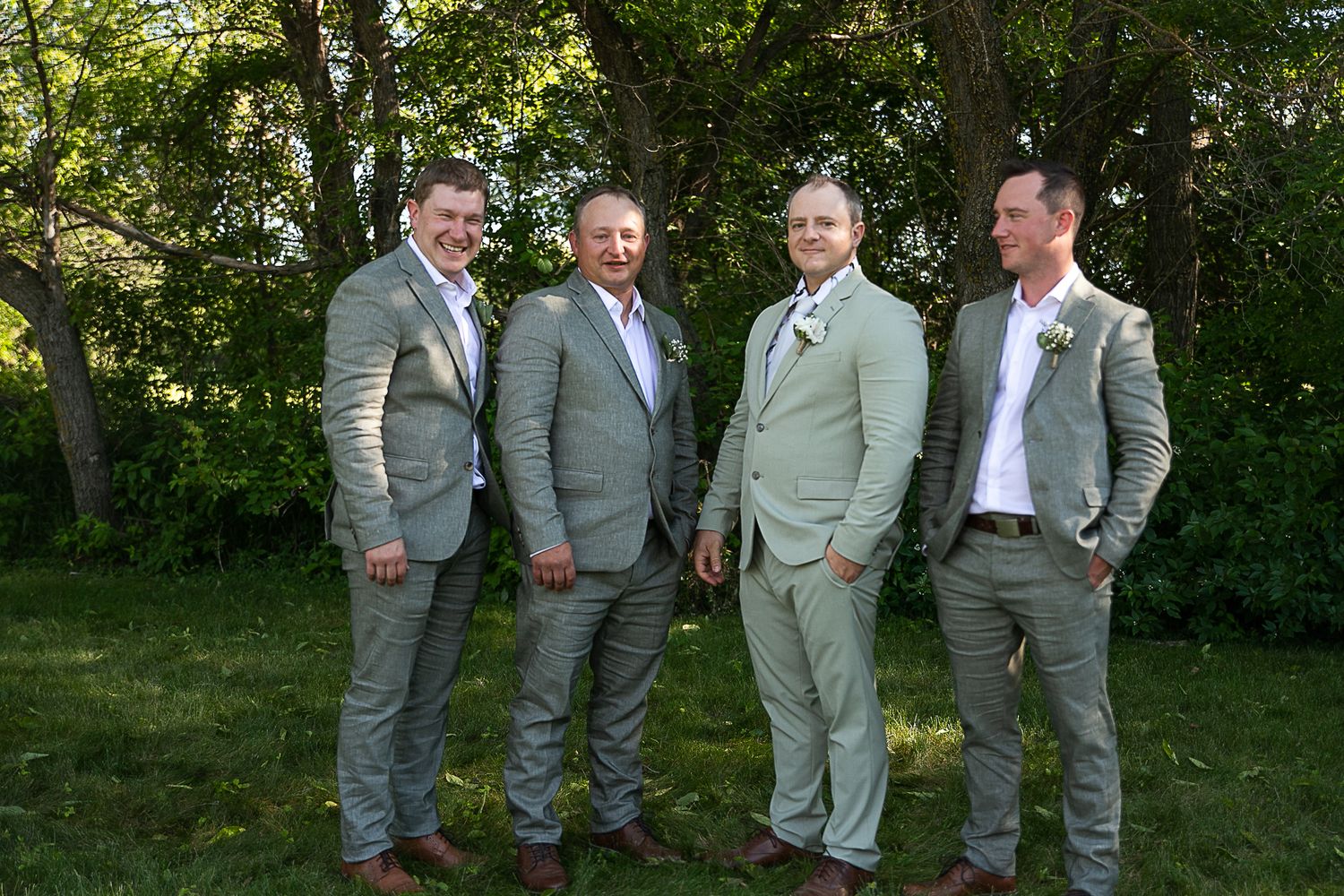 Groomsmen in grey suits gather for casual group photo in outdoor garden setting.