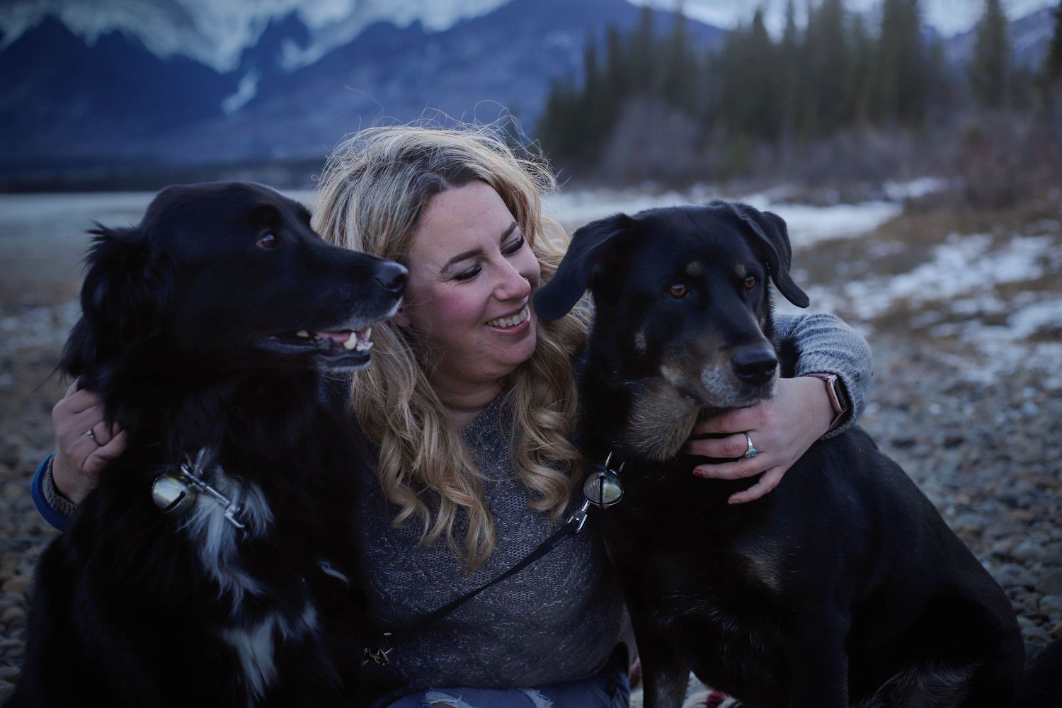 A person and their black dog share affectionate moments against a snowy mountain backdrop.