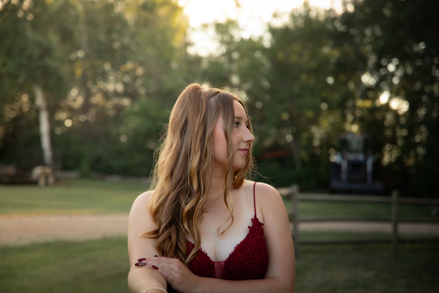 A person in a burgundy dress poses outdoors during golden hour.