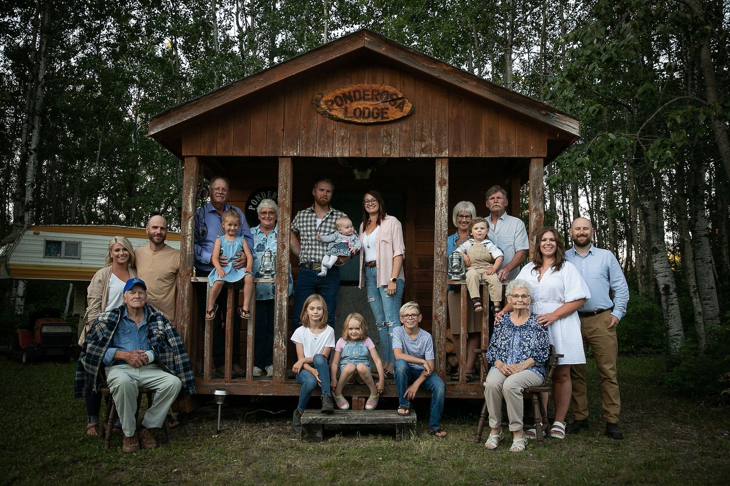 A gathering of people posed on and around a wooden cabin deck in a forest setting.