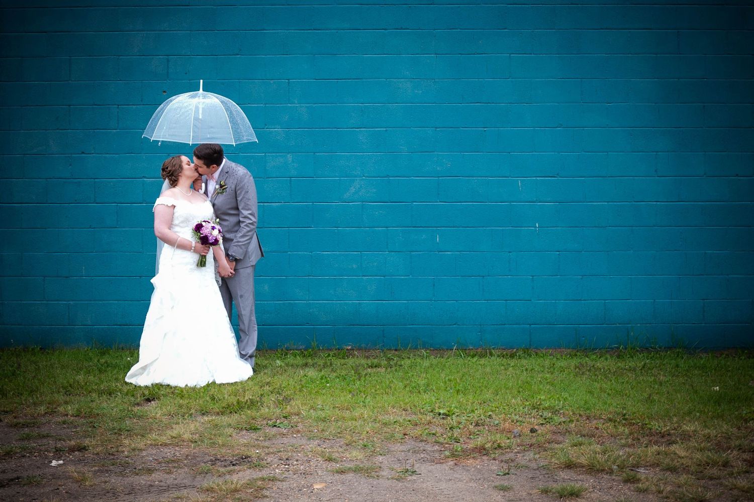 Wedding couple silhouetted against a vibrant turquoise wall outdoors.