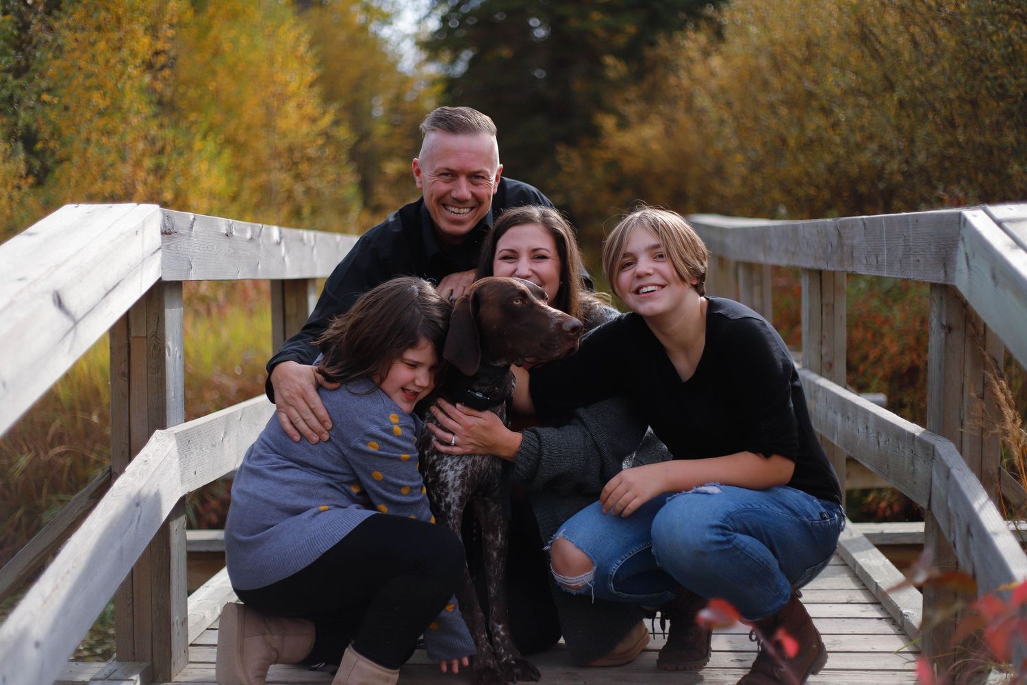 Family laughing together on wooden boardwalk during autumn photo session.