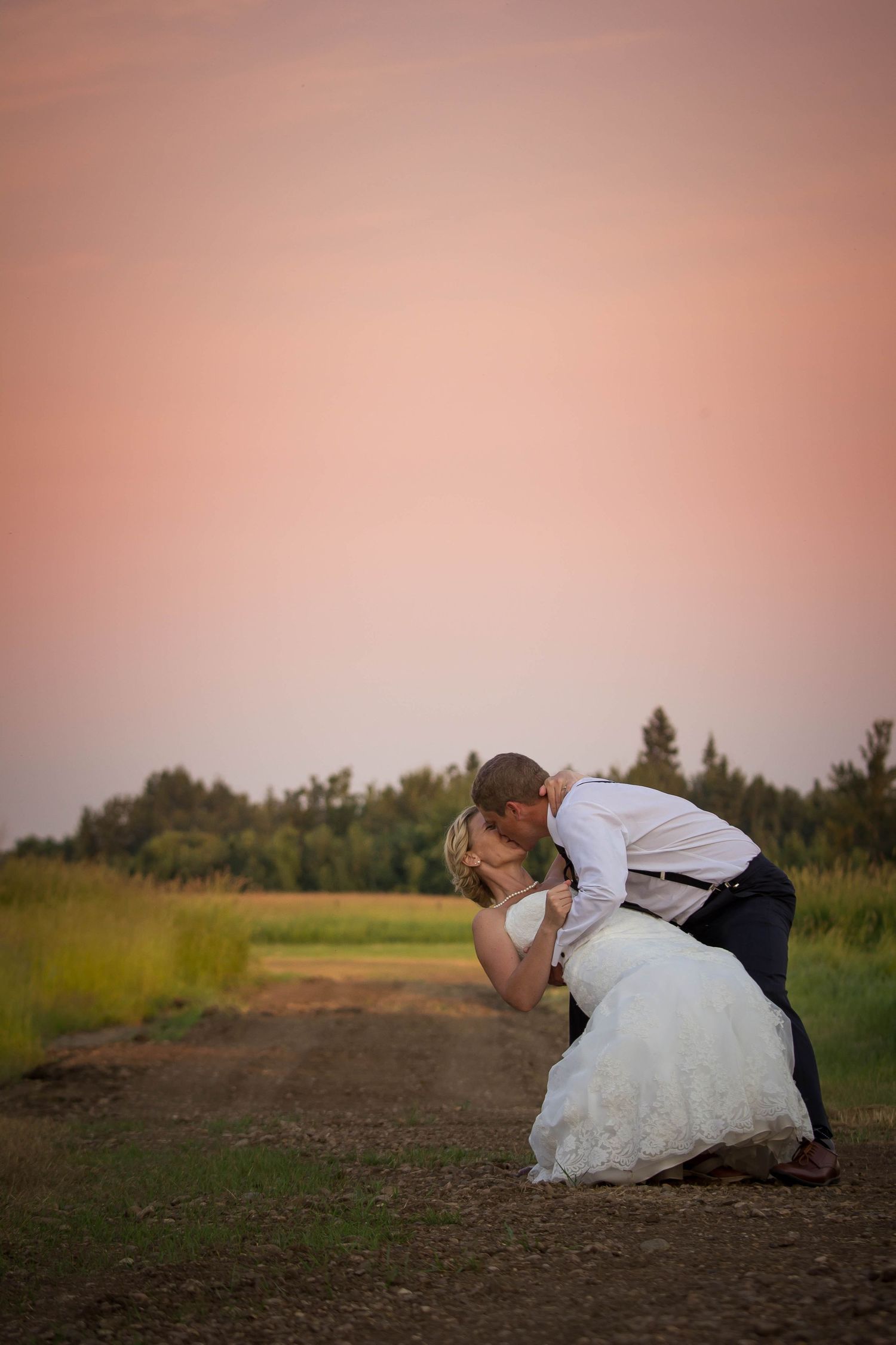 A couple in formal wedding attire lies down in a field at sunset creating a romantic silhouette.