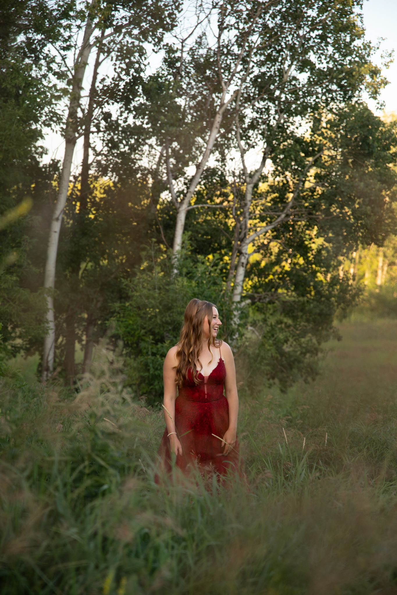 A red formal dress captured among birch trees in warm evening sunlight.