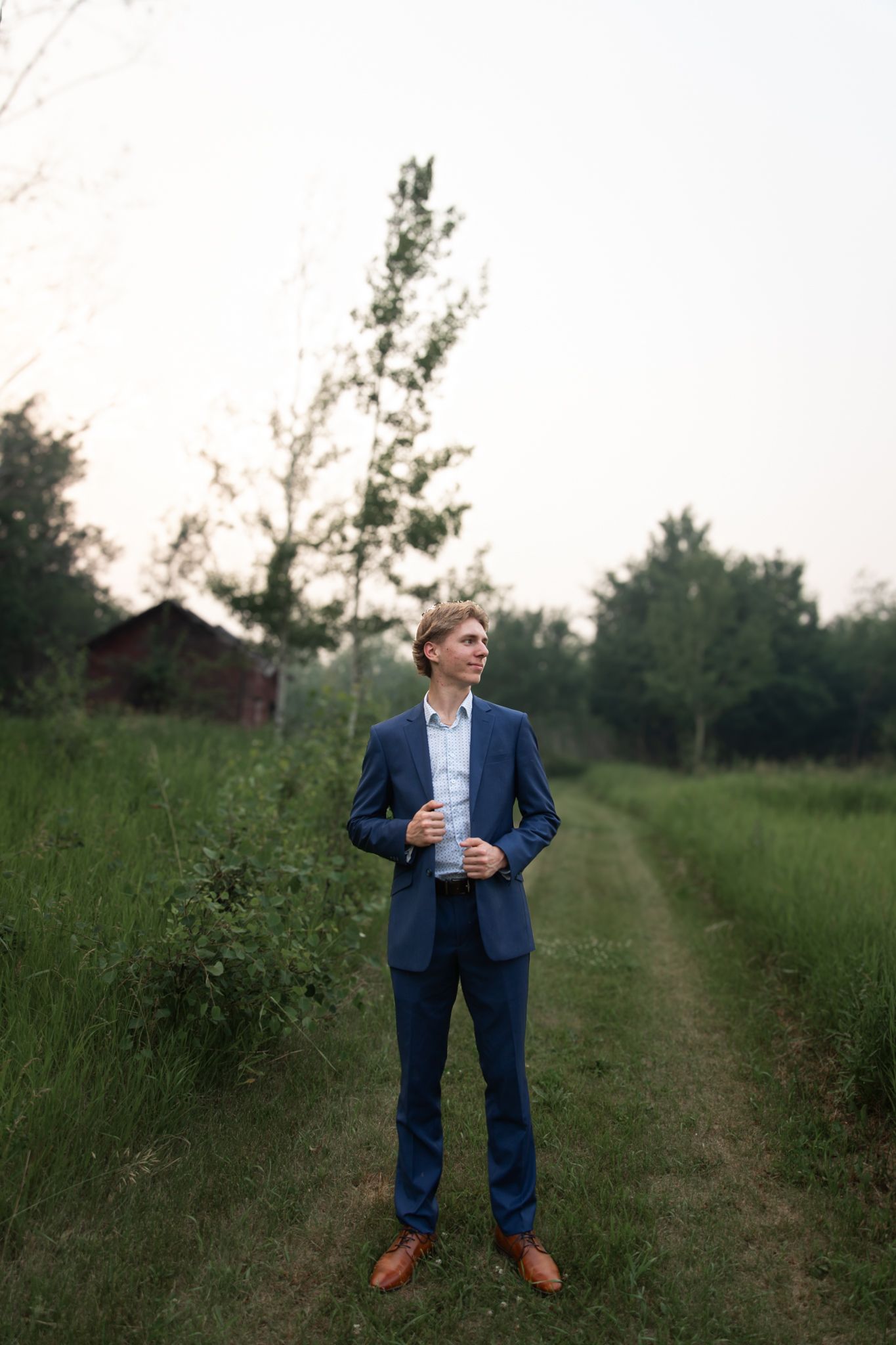 A figure in a blue suit stands on a grassy rural path at sunset.