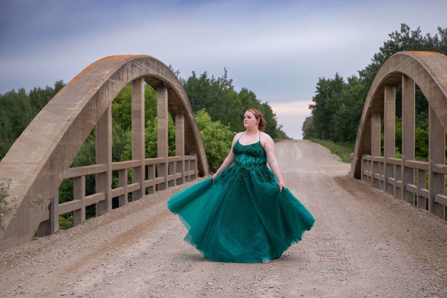 An emerald green ballgown flows dramatically on a rustic wooden bridge.