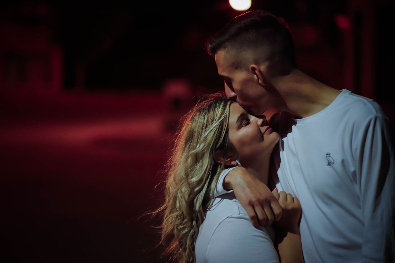 Intimate romantic moment captured under dramatic red lighting.