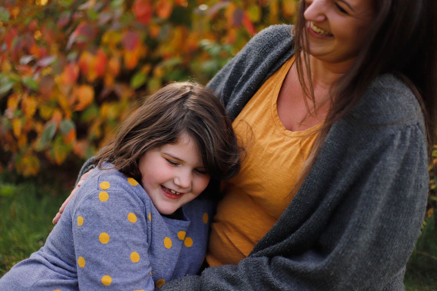 Two people share a tender moment while sitting outdoors against autumn foliage.