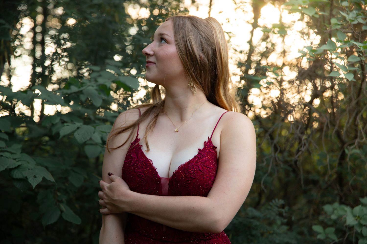 A burgundy lace gown photographed against lush greenery at sunset.