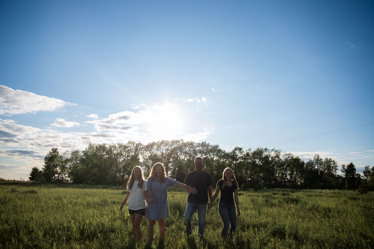 A group poses in a sunlit field with trees and blue sky in the background.