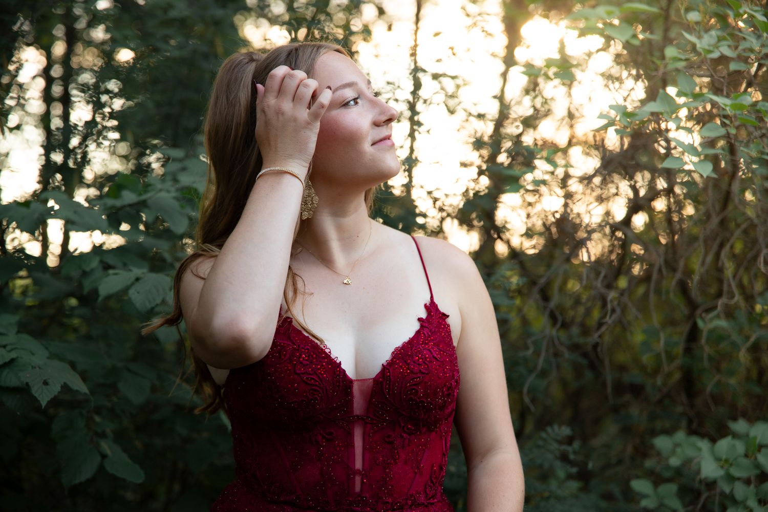 A candid portrait in a deep red formal dress against a natural forest backdrop.
