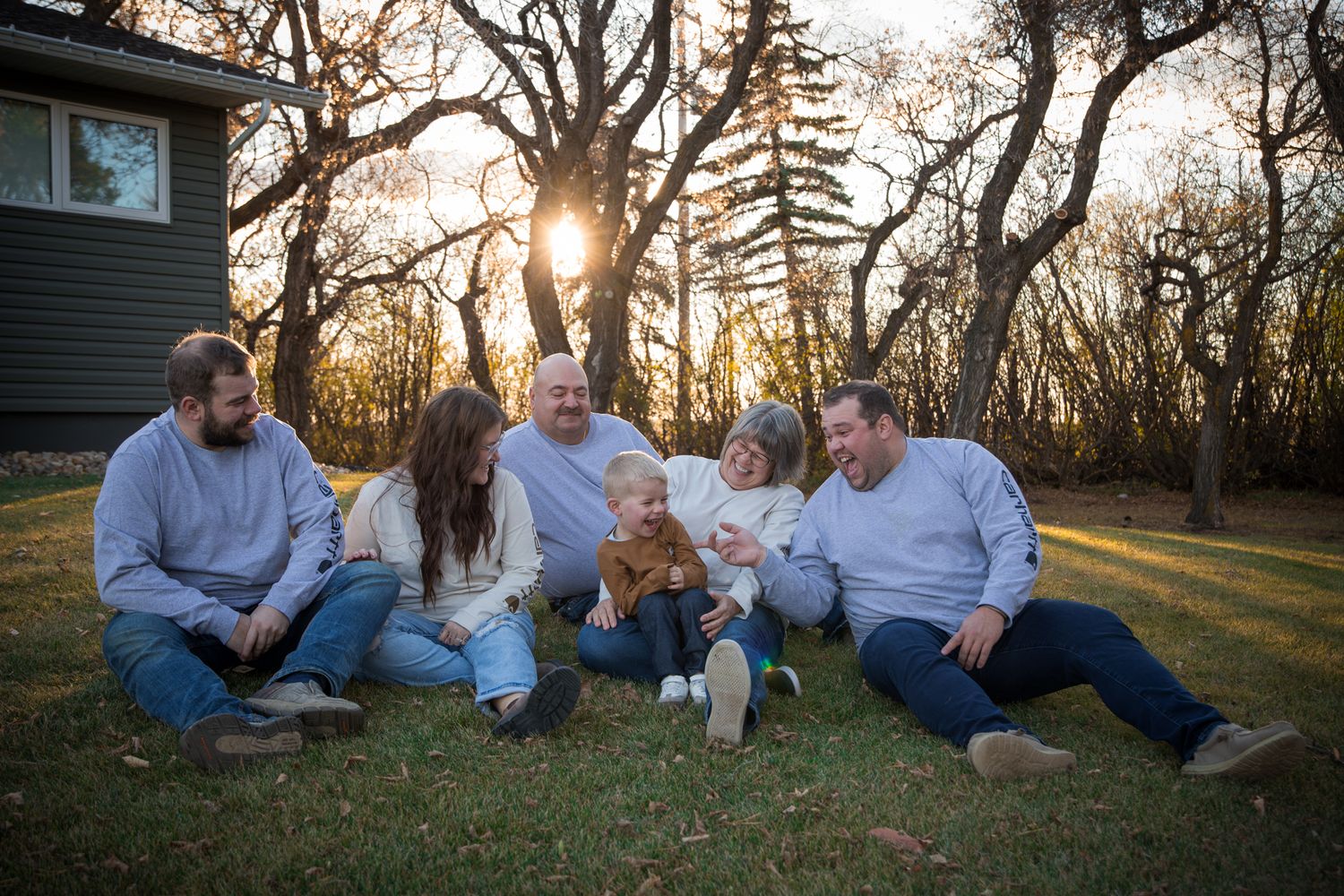 Family members arranged in casual poses on grass during golden hour photography session.