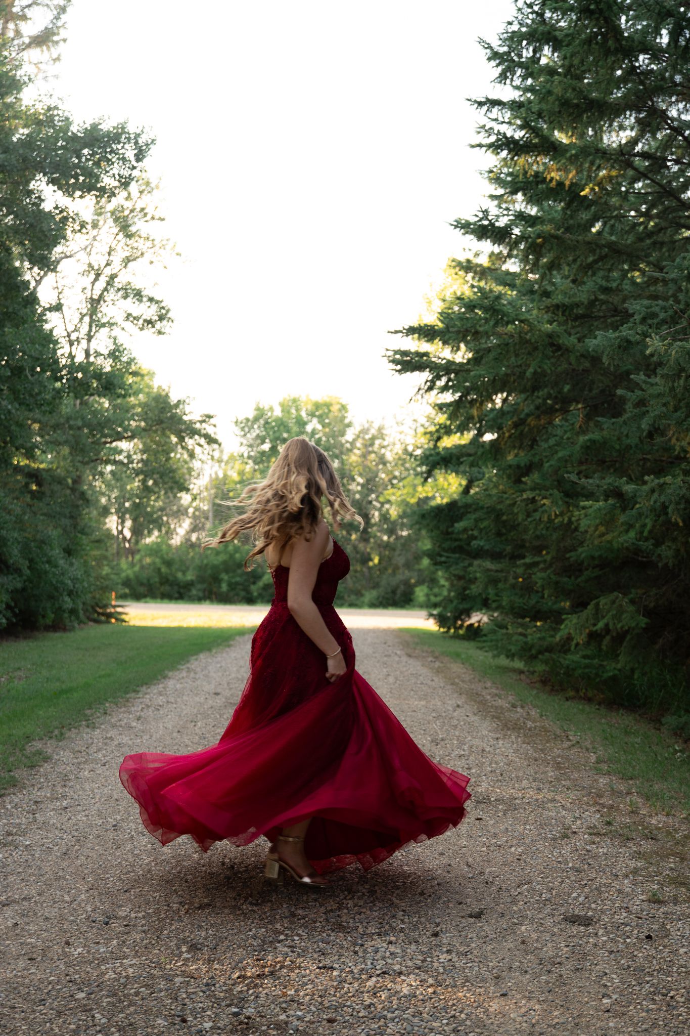 A flowing red dress twirls dramatically on a tree-lined path at sunset.
