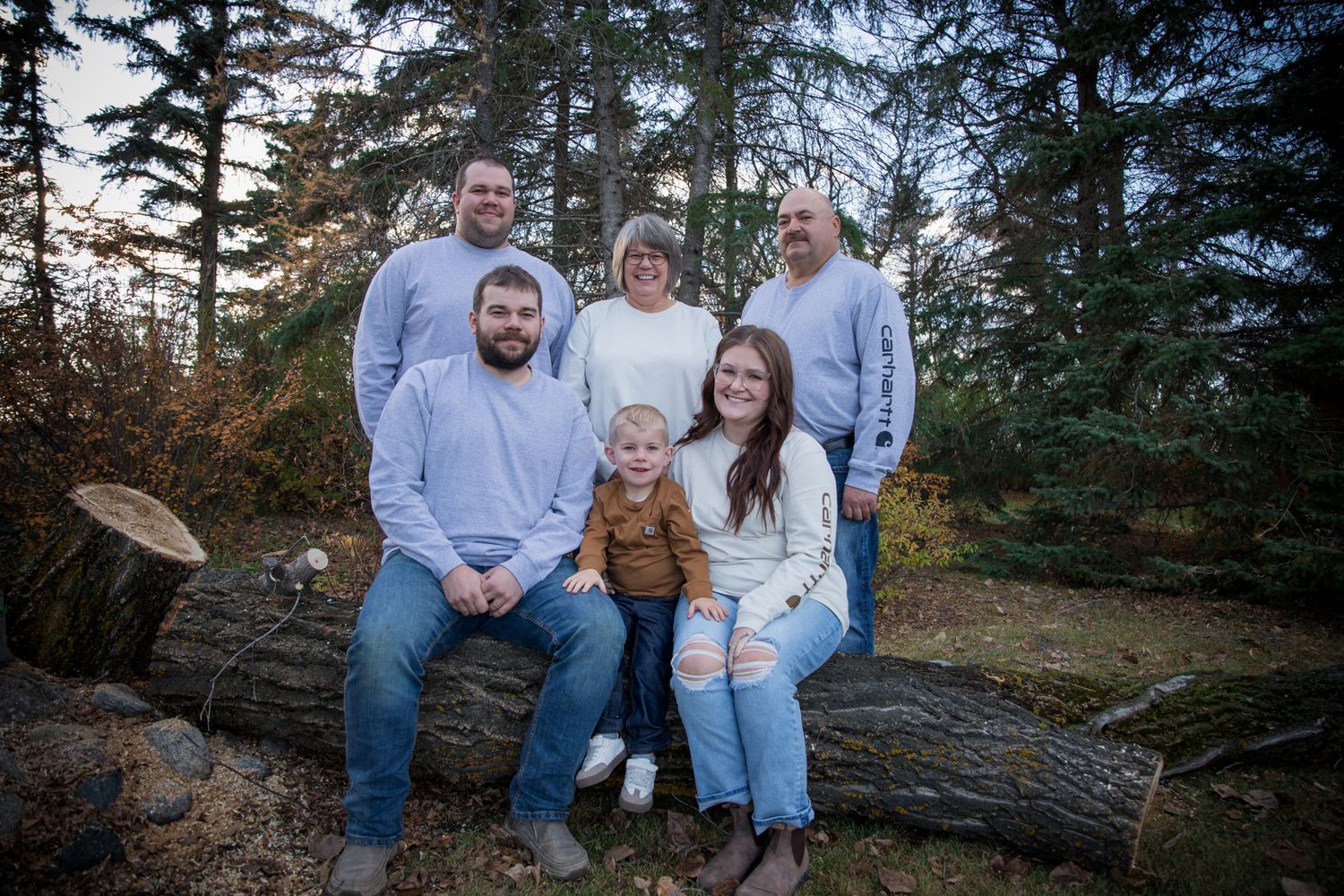 A casual outdoor family photoshoot in a wooded area during autumn with coordinated light colored clothing.