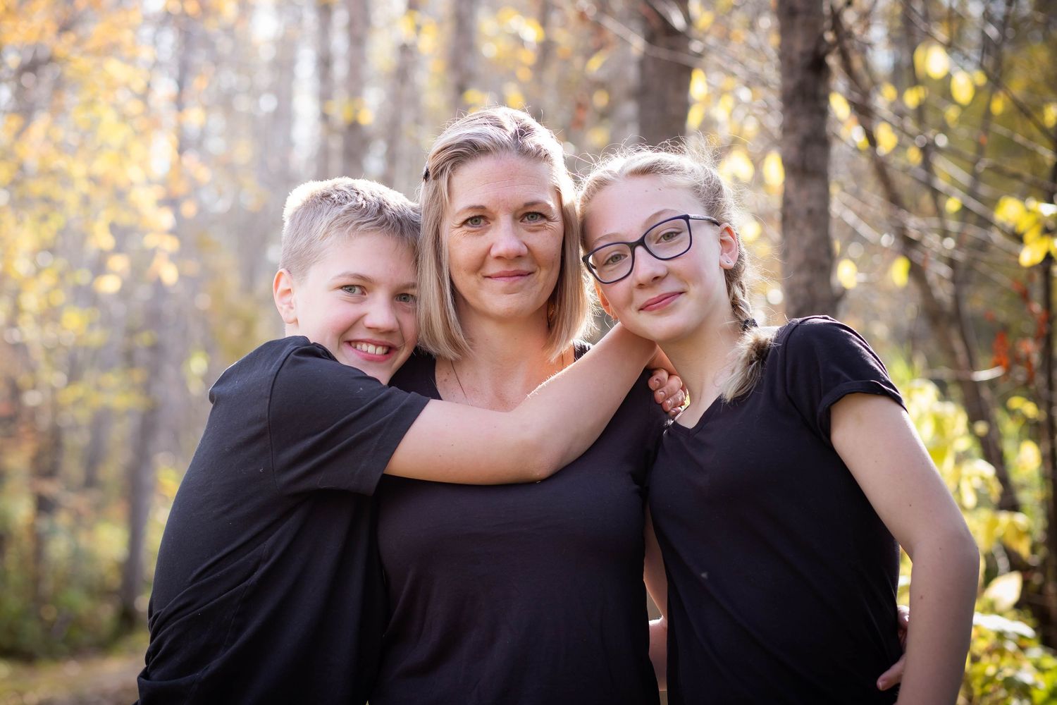 Three people pose together outdoors with autumn trees in the background.