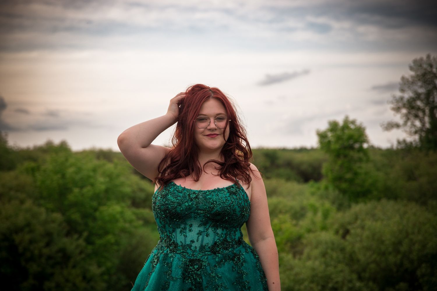 Flowing emerald dress captured against moody sky in outdoor portrait session.