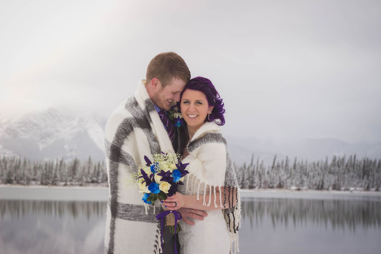 Winter wedding couple shares a romantic moment in a snow-covered landscape with blue bouquet.
