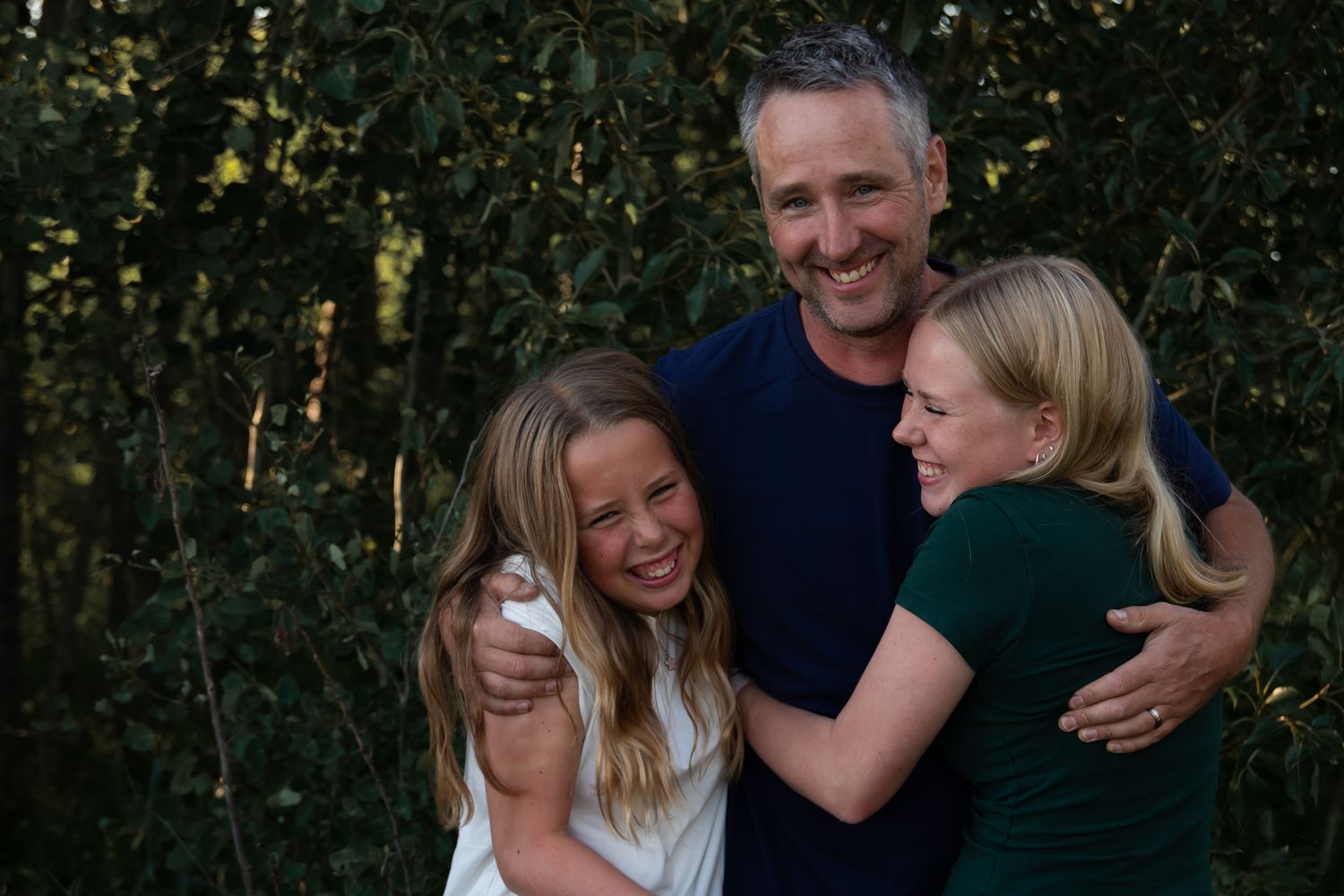 A group shares a joyful moment of laughter and hugs in a wooded setting.