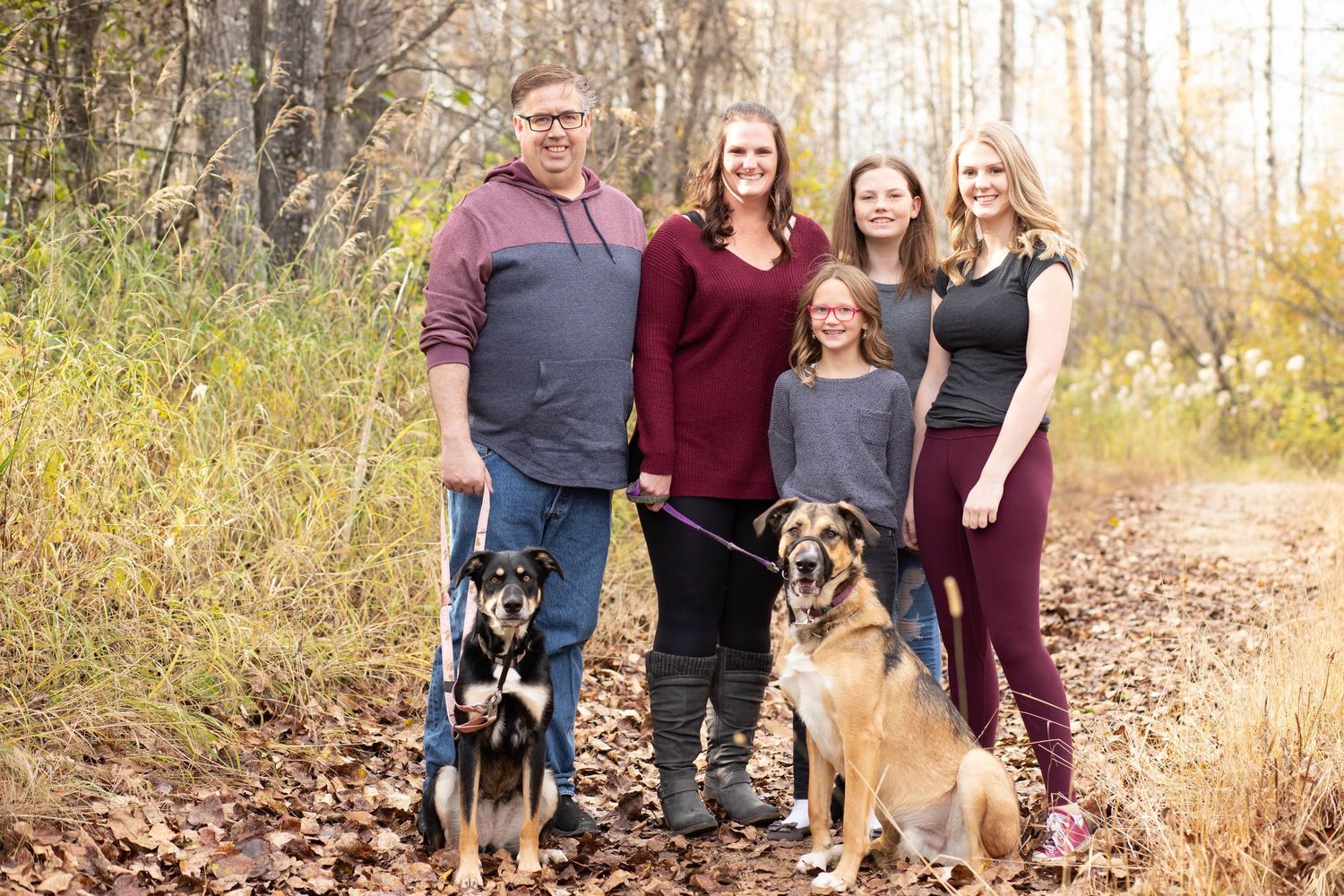 Family and pets posing together on a nature trail during fall season.