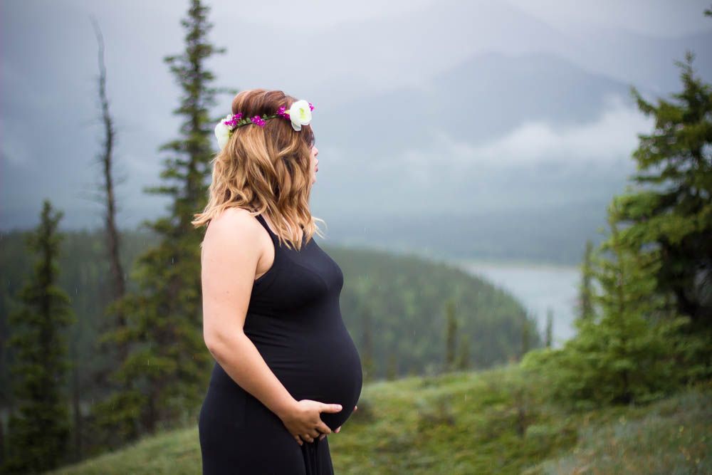 Maternity photo shoot with mountain lake and evergreen forest backdrop.