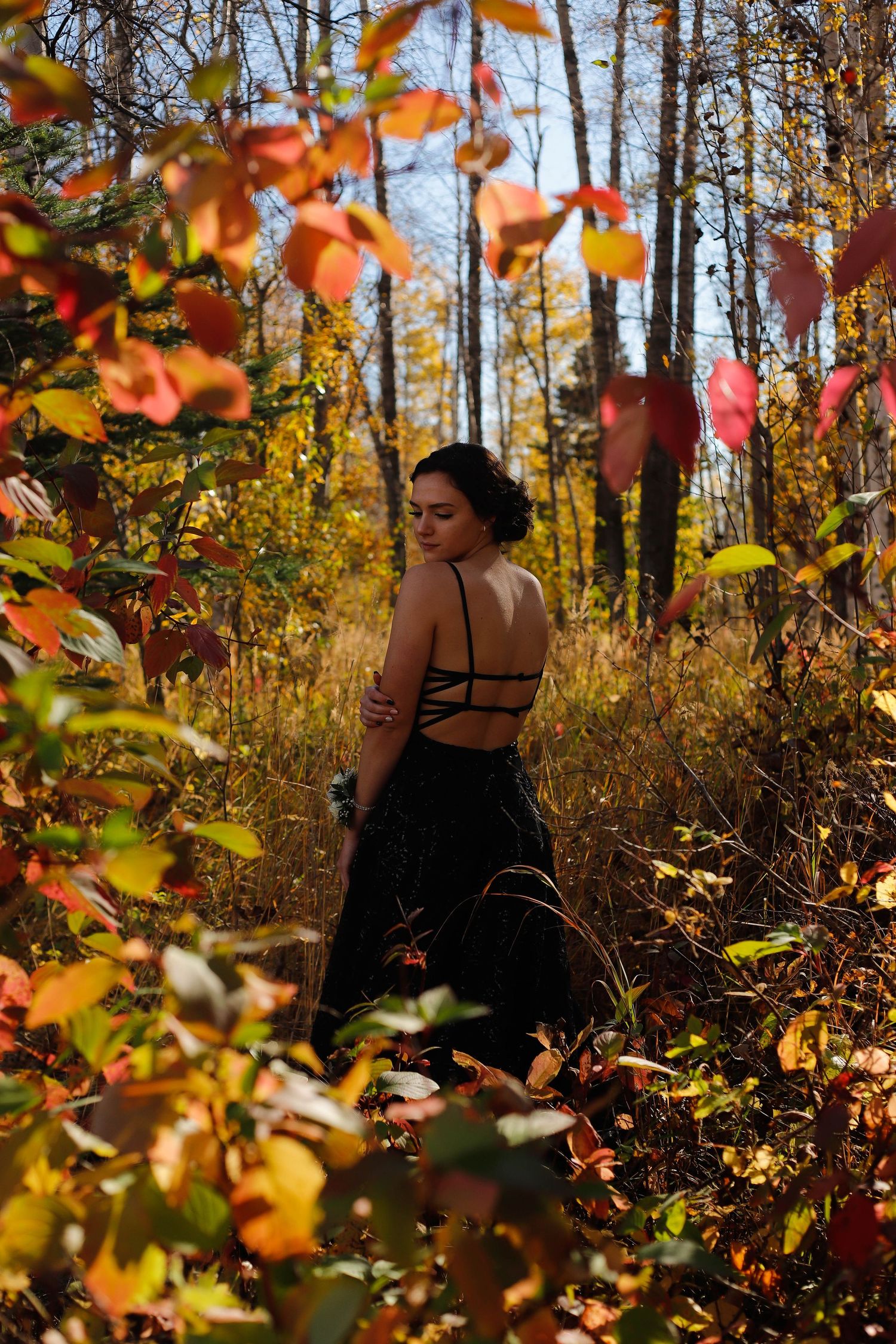 Figure in black dress surrounded by vibrant autumn foliage in sunlit forest.