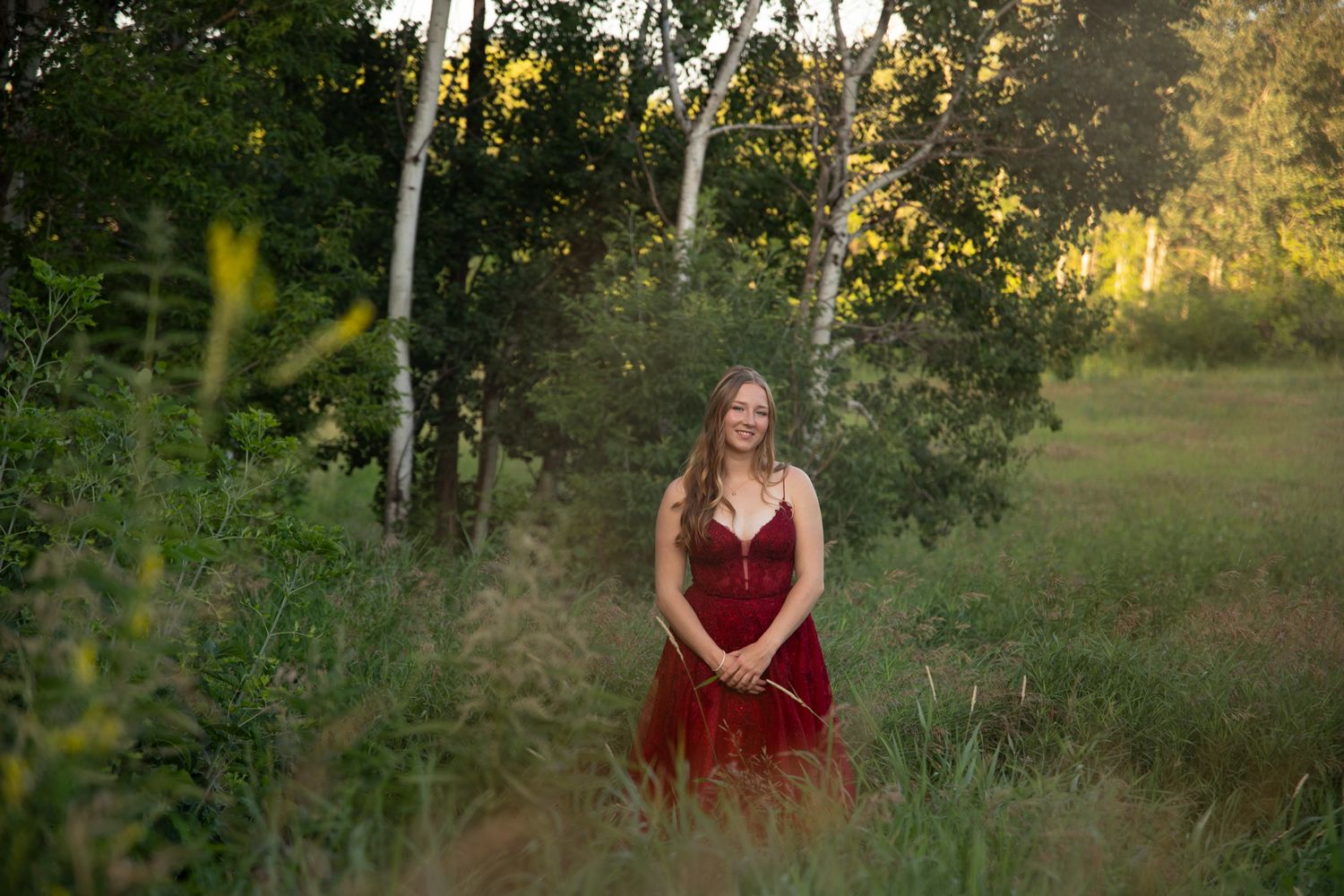 A burgundy evening gown photographed in a golden-lit natural setting.