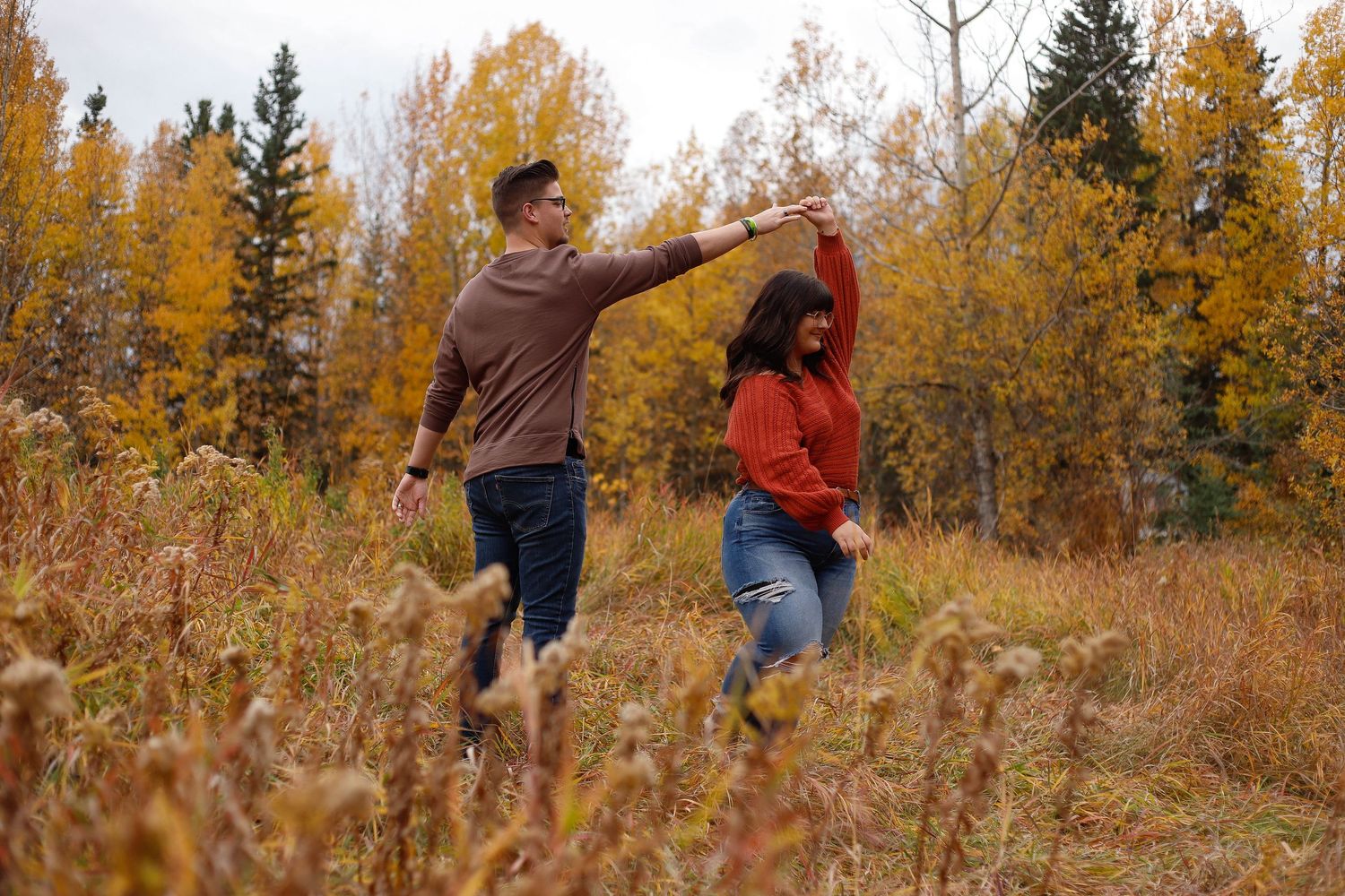 A couple poses playfully on a wooden bridge with fall foliage creating a scenic backdrop.