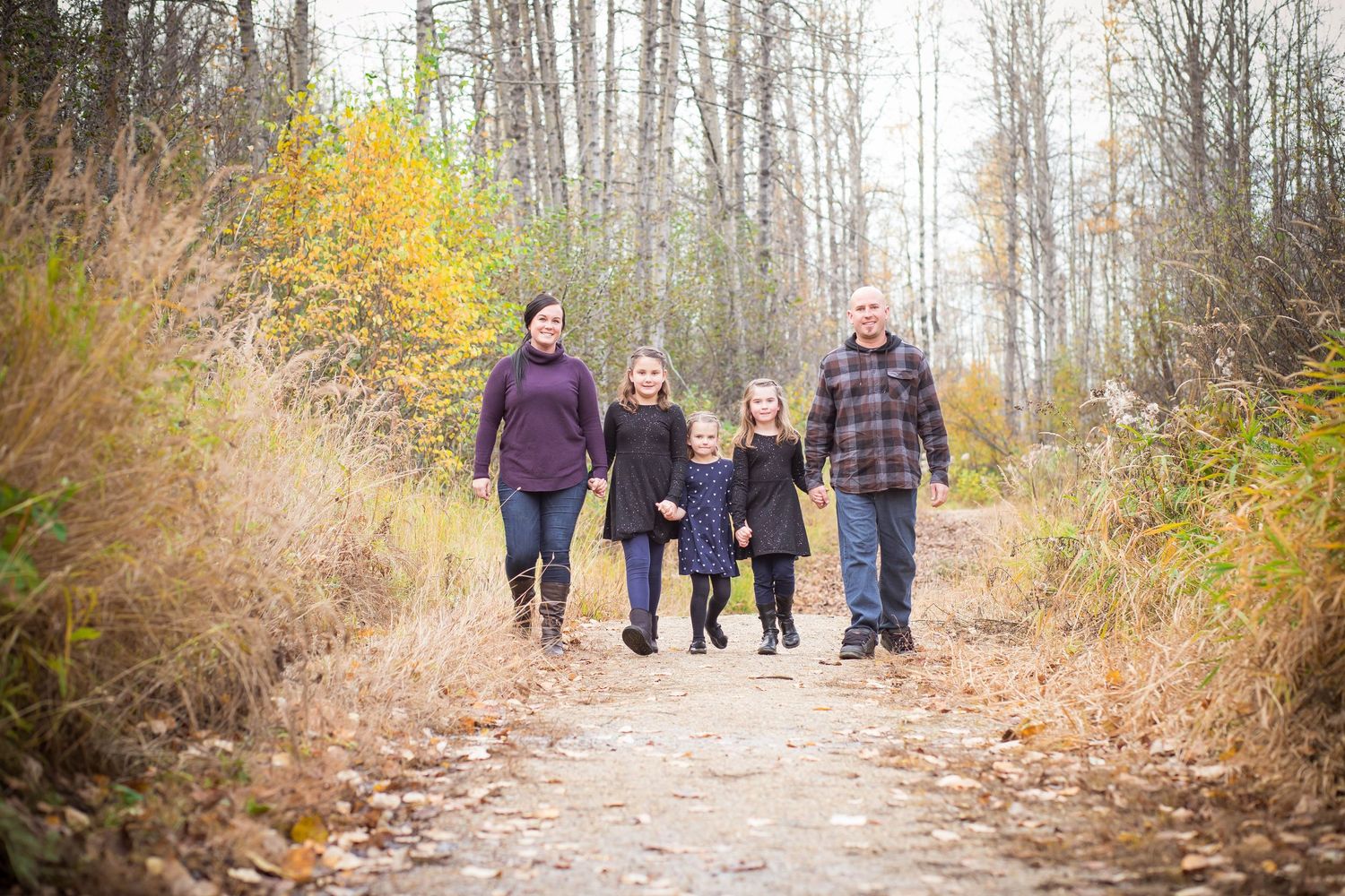 Family of four walking together on a nature trail surrounded by fall foliage.