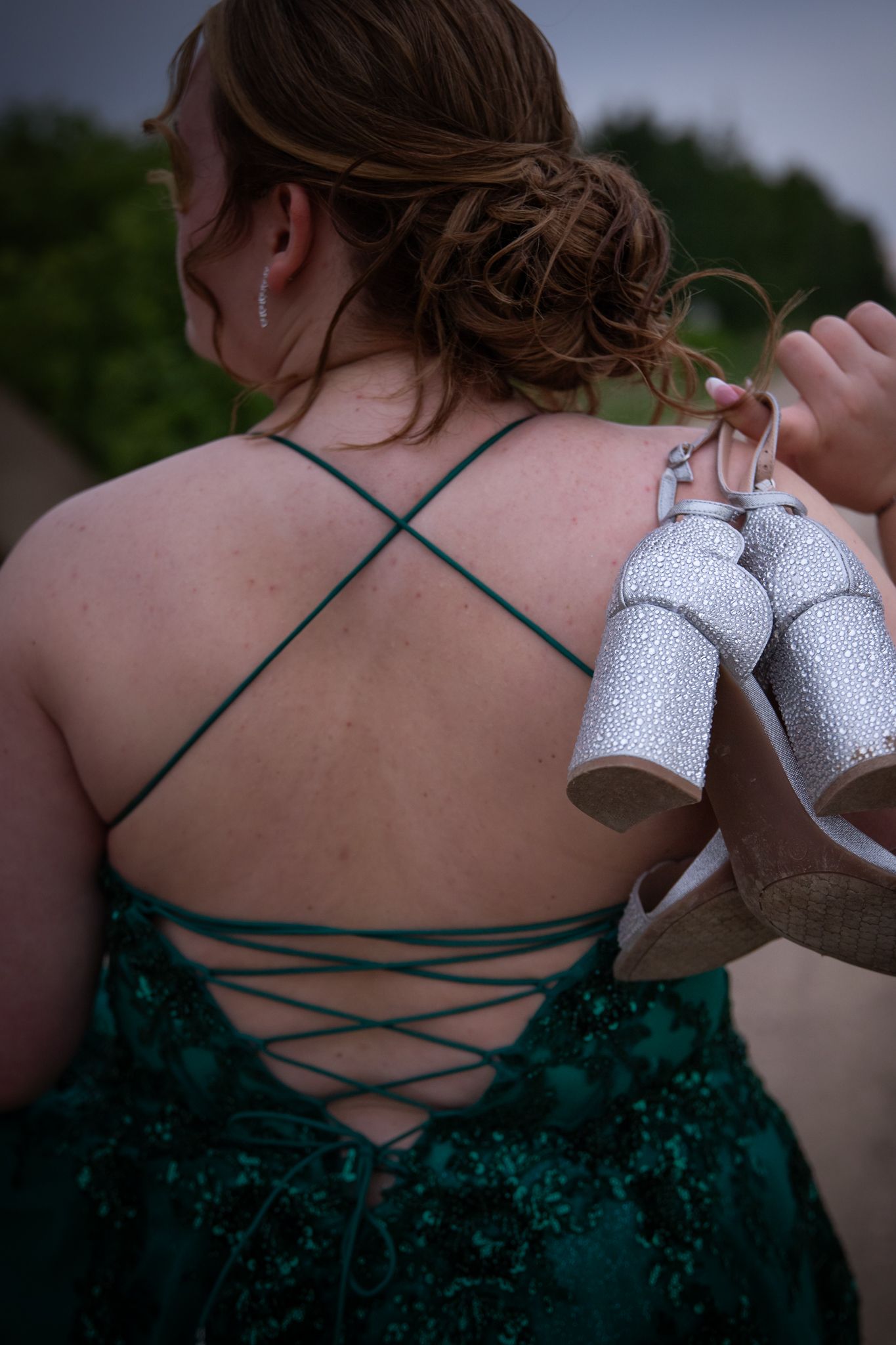 A person in a green lace-up dress holds white shoes while showing the criss-cross back detail.