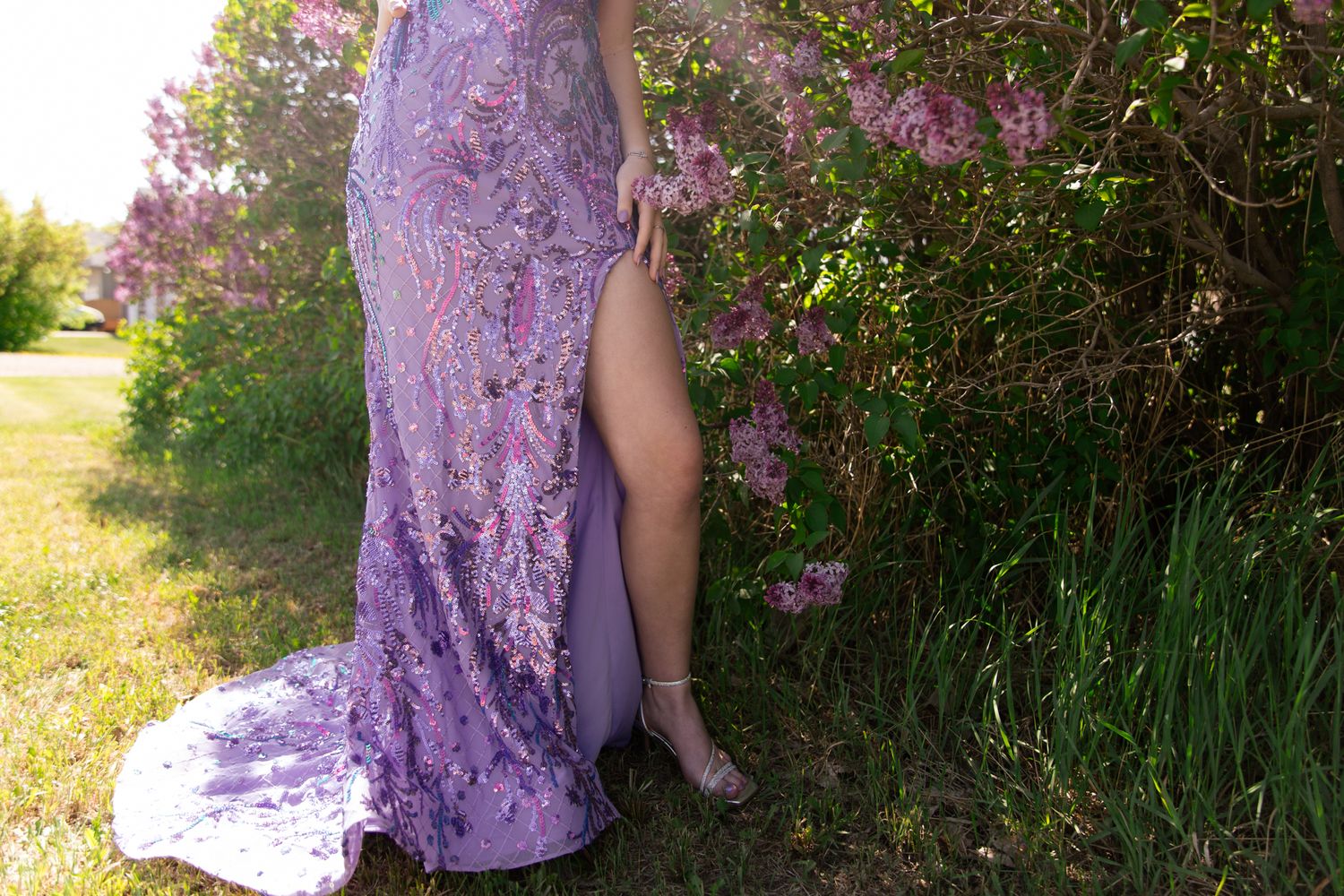 A purple sequined gown photographed against flowering bushes in natural outdoor lighting.