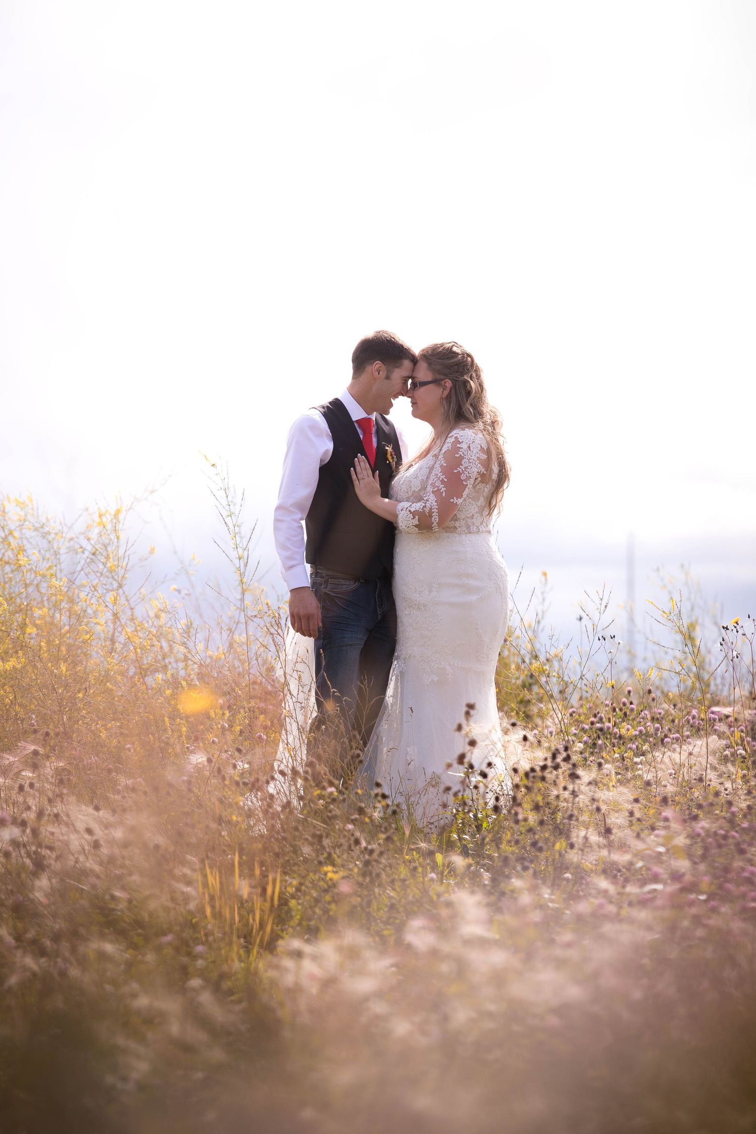 Romantic wedding couple embracing in a sunlit field of wildflowers during golden hour.