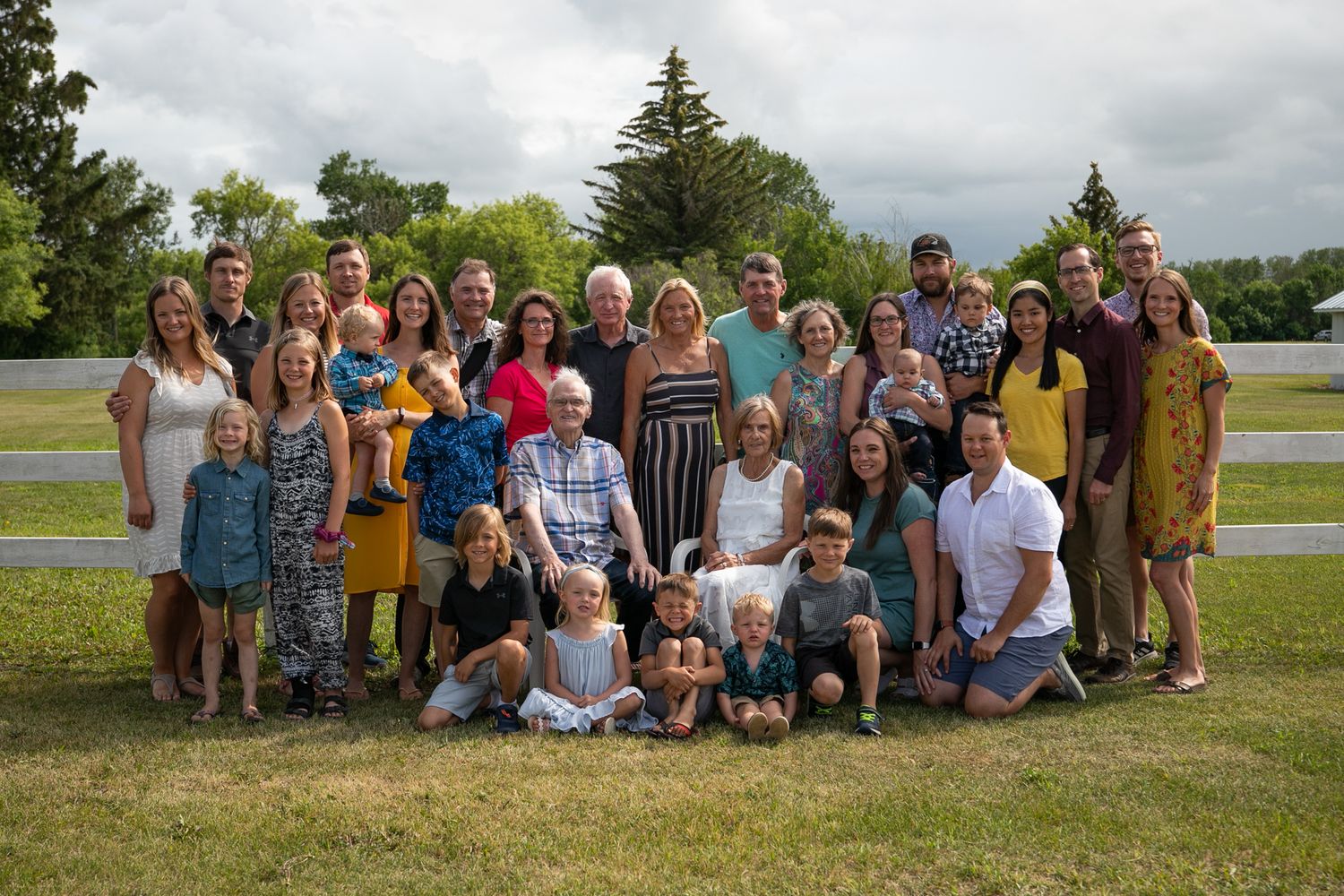 Large extended family group photo outdoors with trees and cloudy sky in background.