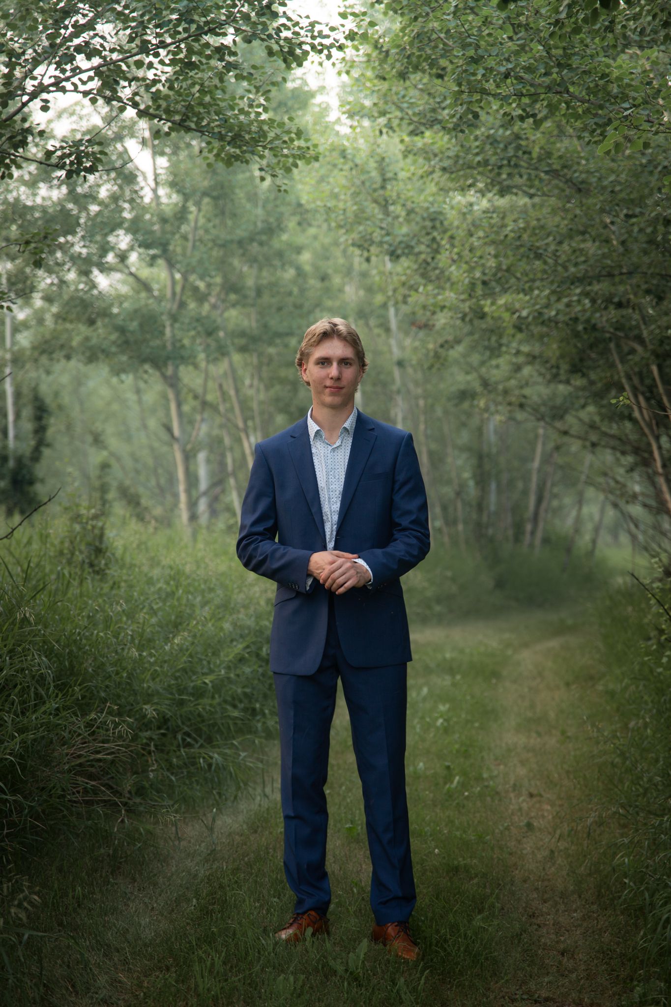 A professional portrait taken on a rustic trail surrounded by trees and foliage.
