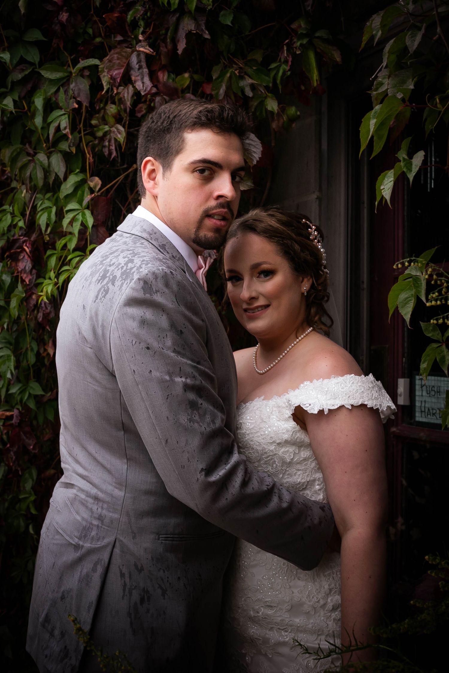 Wedding couple poses intimately against ivy-covered wall.