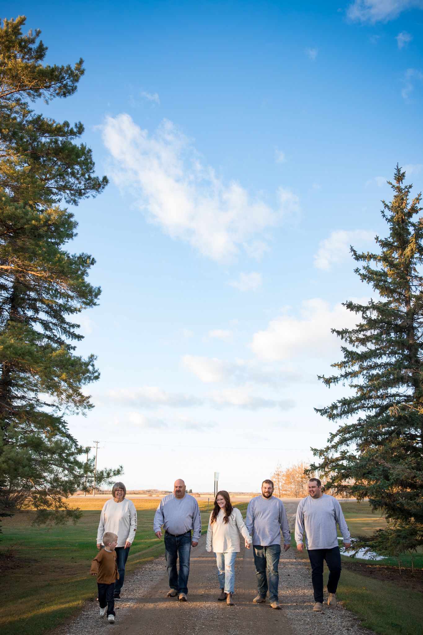 Family walking together against blue sky and evergreen trees during outdoor photo session.