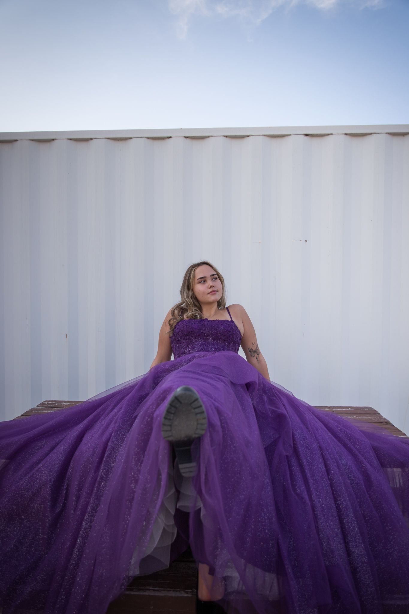 A dramatic purple ball gown spread across a bench against a white wall.