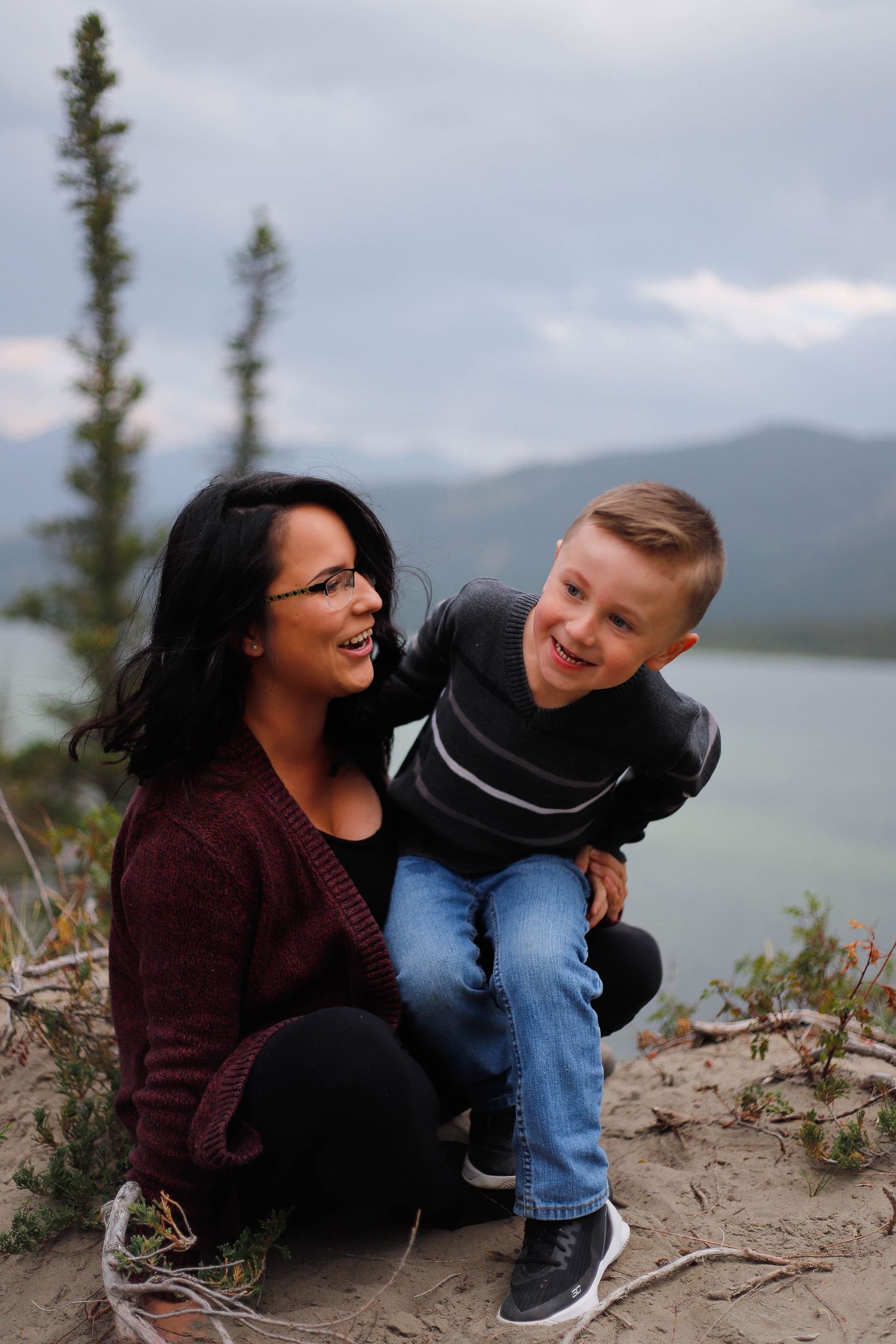 Playful interaction between parent and child on rocky overlook with lake view.