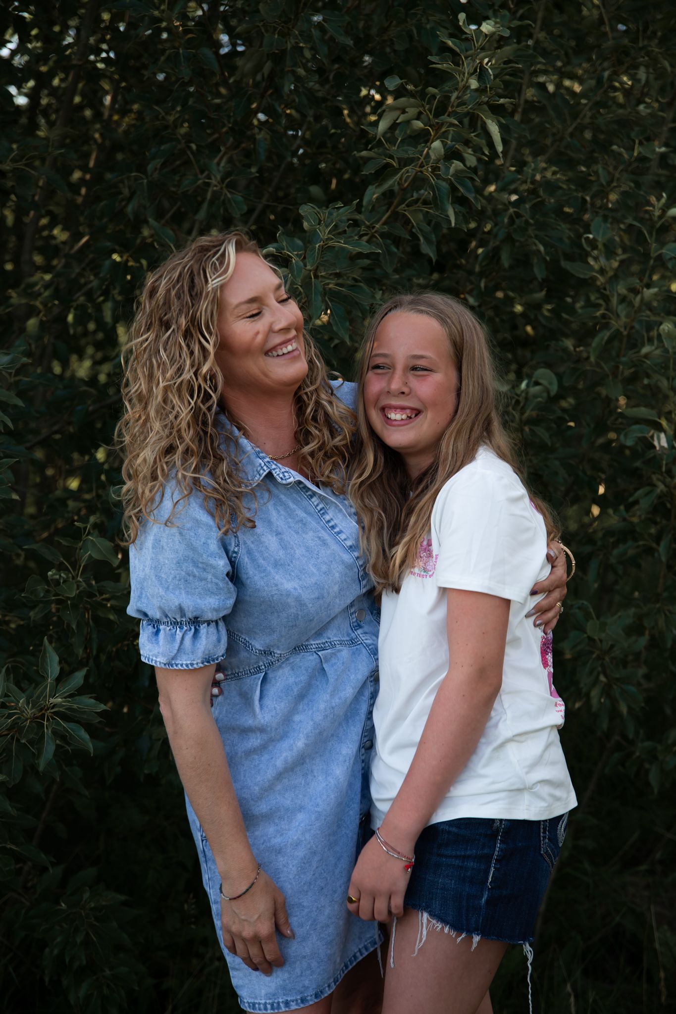 Two people share a joyful embrace while laughing outdoors against a green foliage background.
