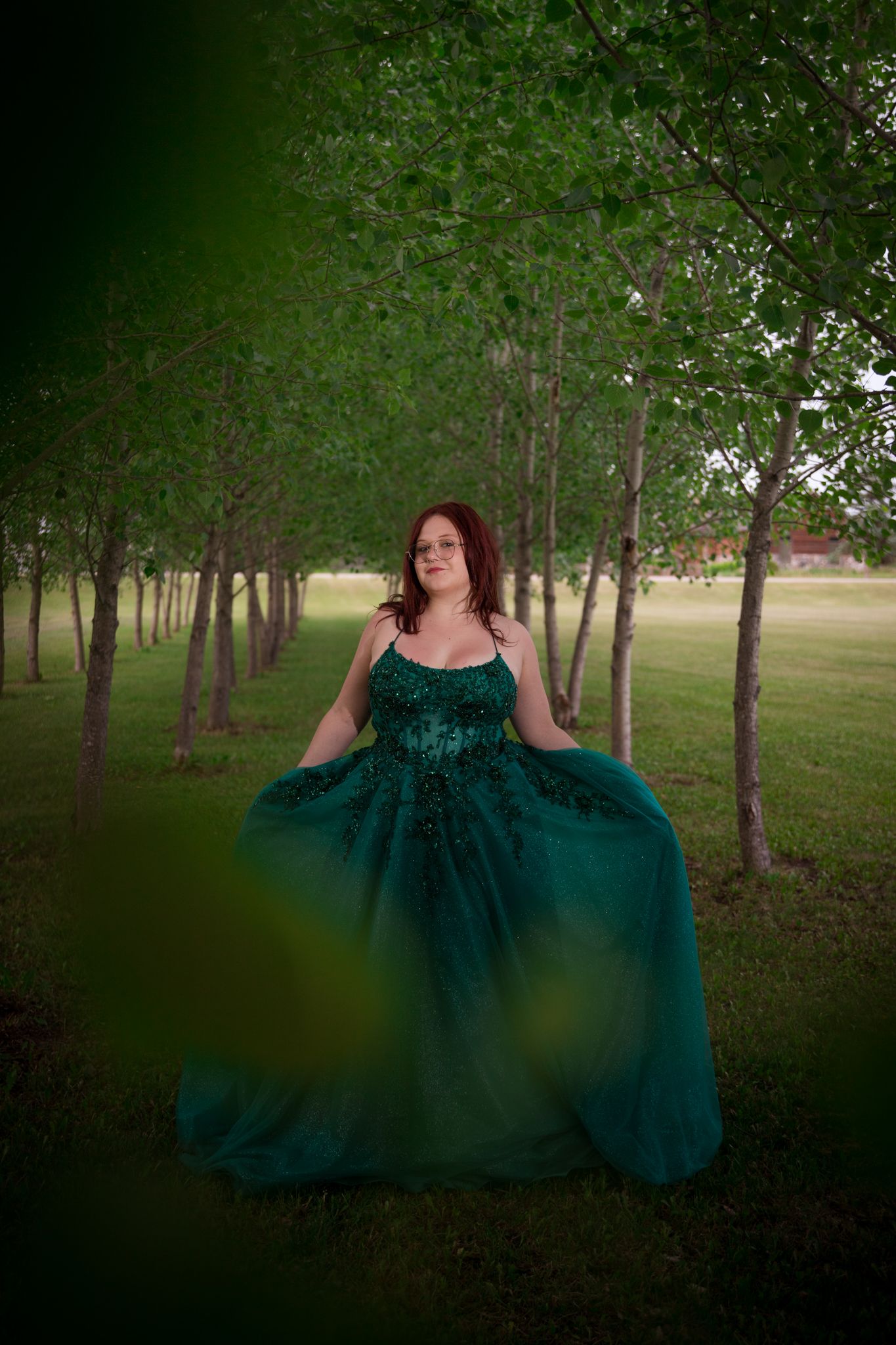 An elegant emerald gown with sparkly details captured in a natural woodland setting at dusk.