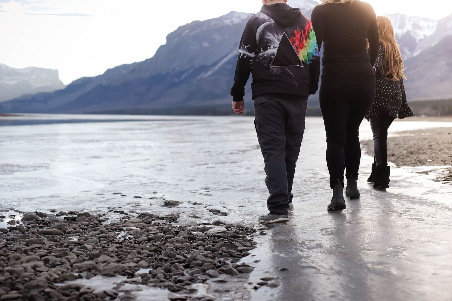 Group walking along a rocky beach with mountains in the background during winter.