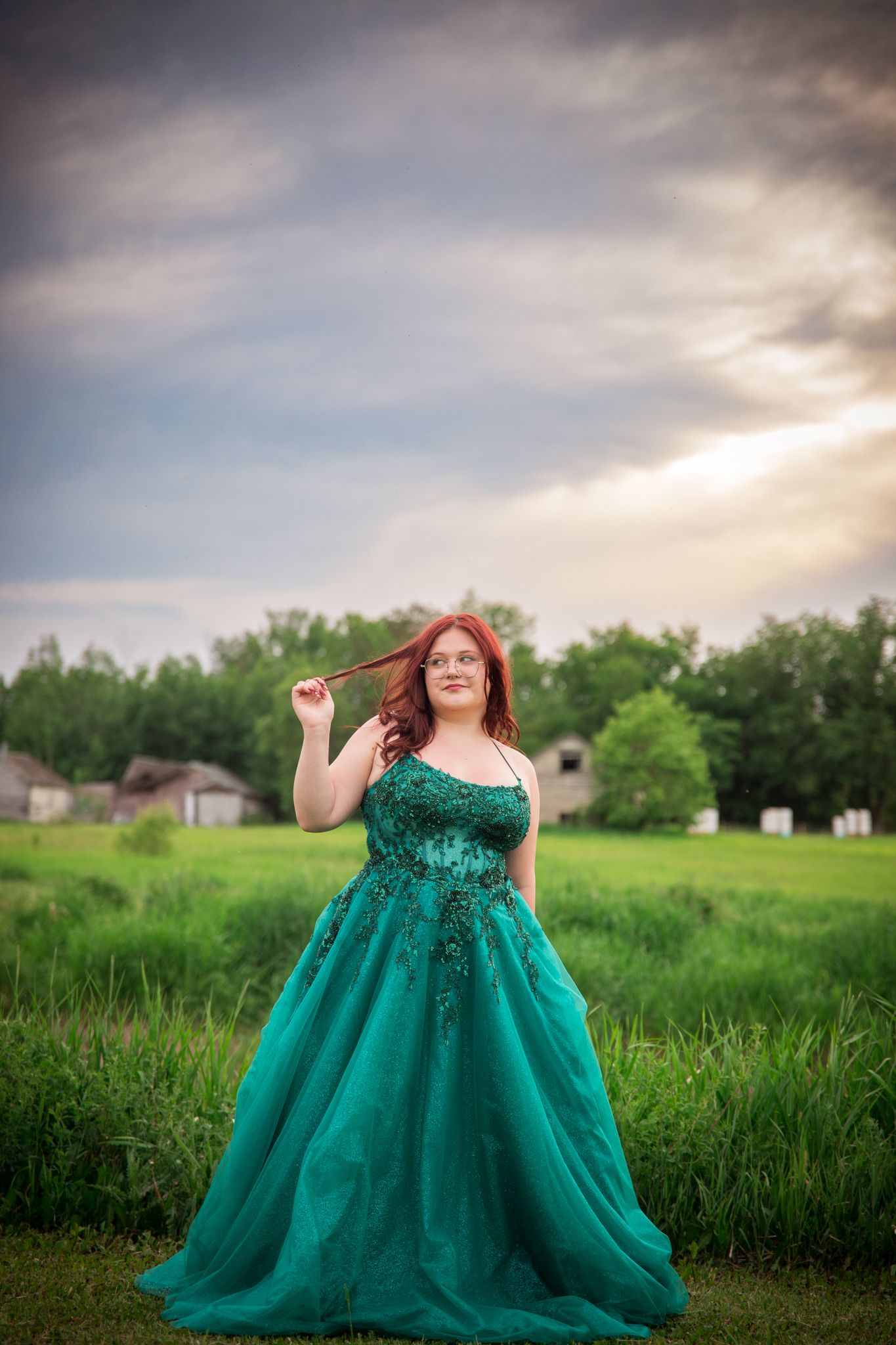 Dramatic emerald ballgown photographed in open field under stormy summer sky.