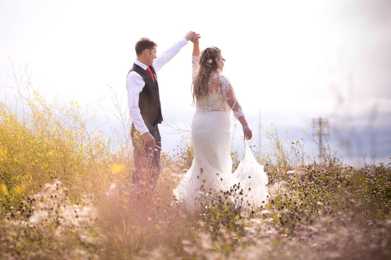 Couple dancing together in a field of yellow wildflowers at sunset.