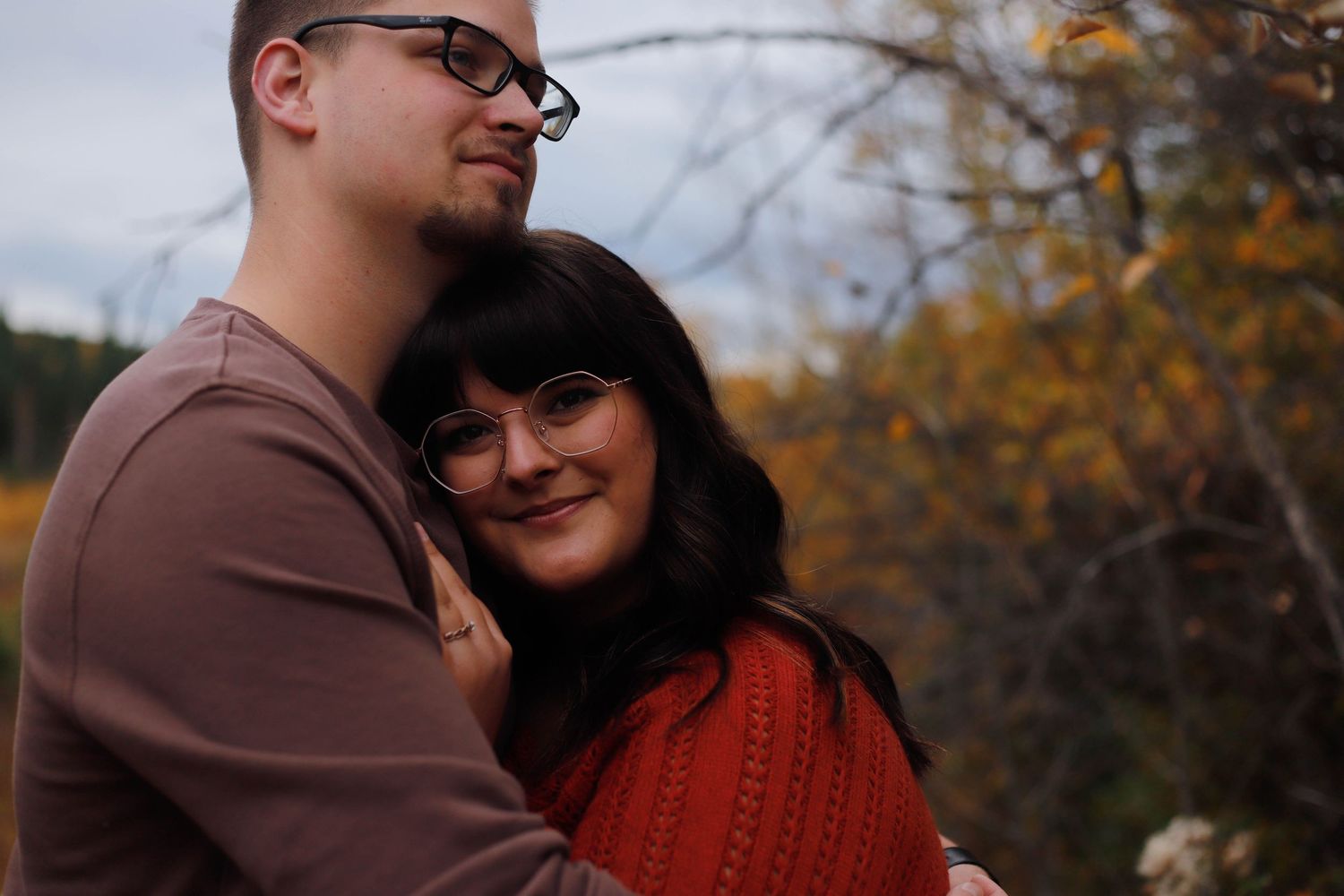 A couple embraces on a wooden bridge surrounded by autumn foliage and golden trees.