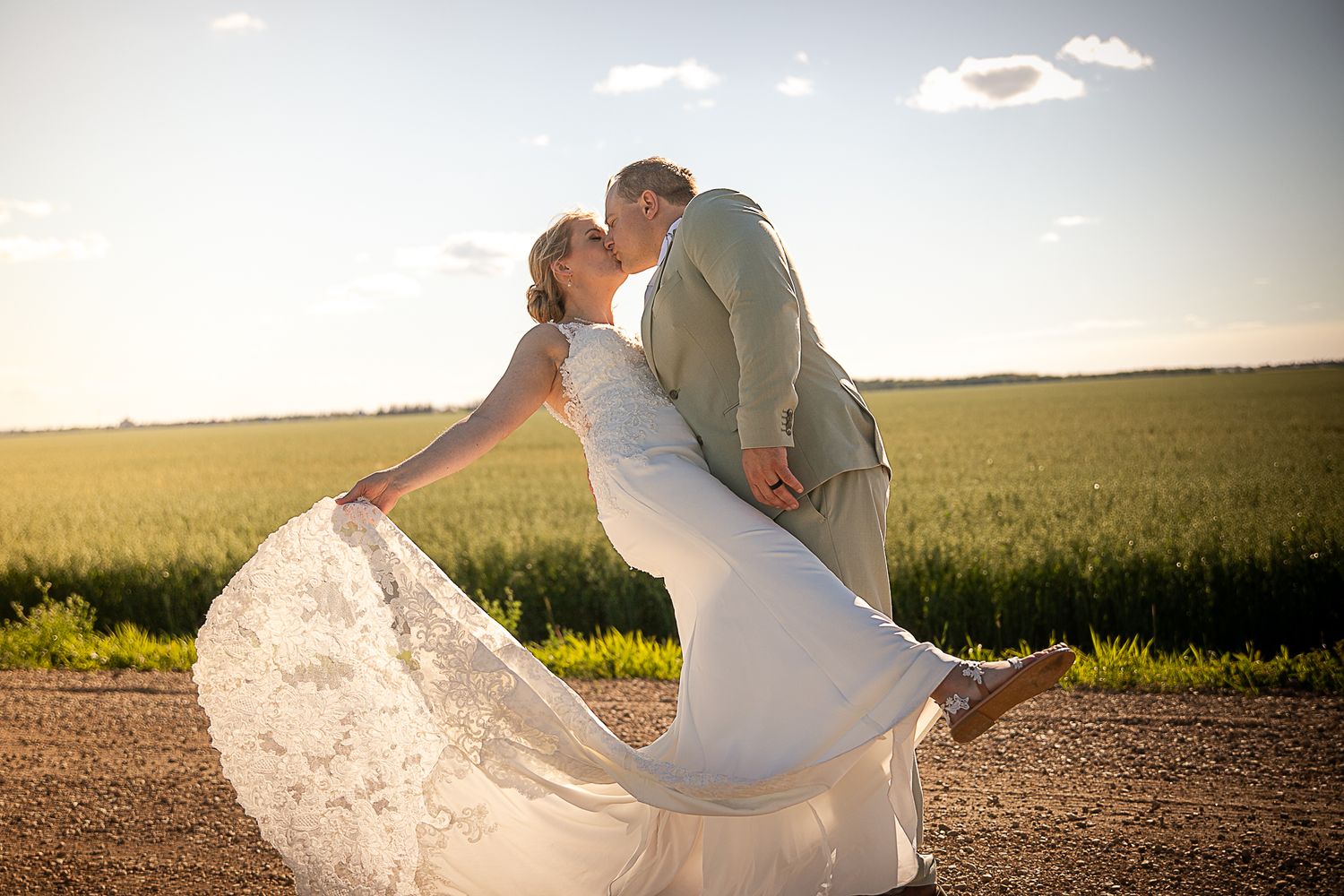 Newlyweds embrace in golden wheat field at sunset.